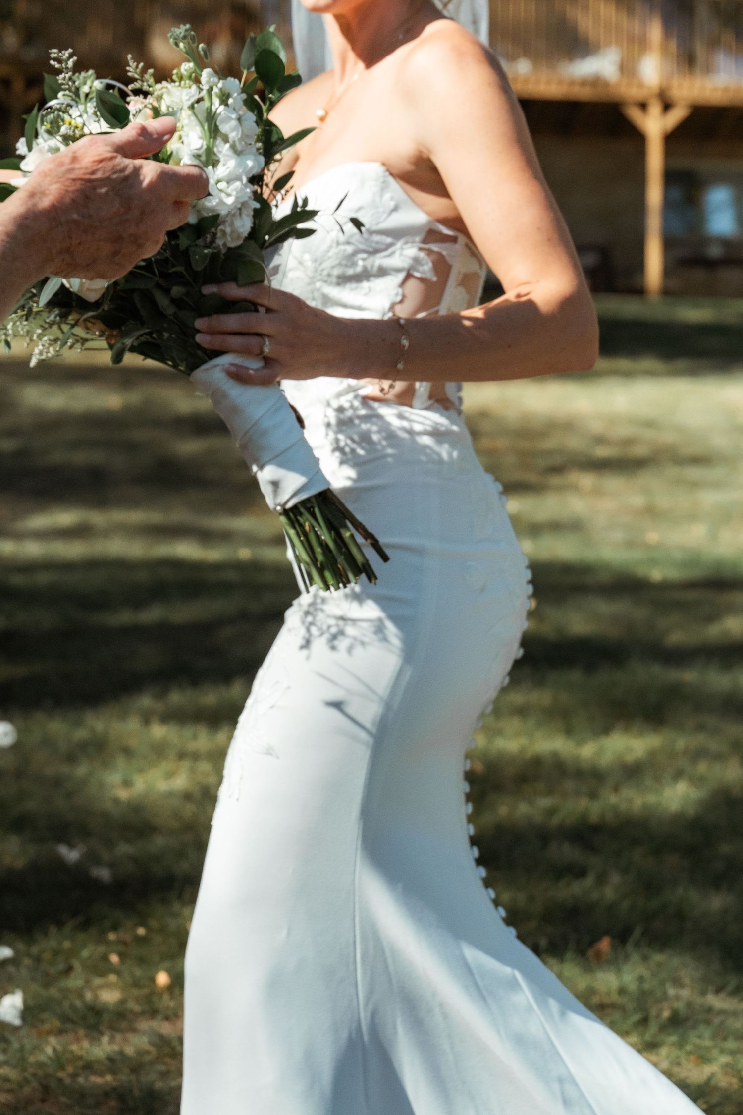 Bride in fitted white wedding dress twirling outdoors holding a floral bouquet.