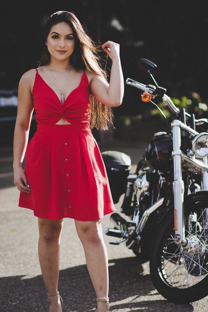 girl in red dress playing with hair, in front of road motorcycle