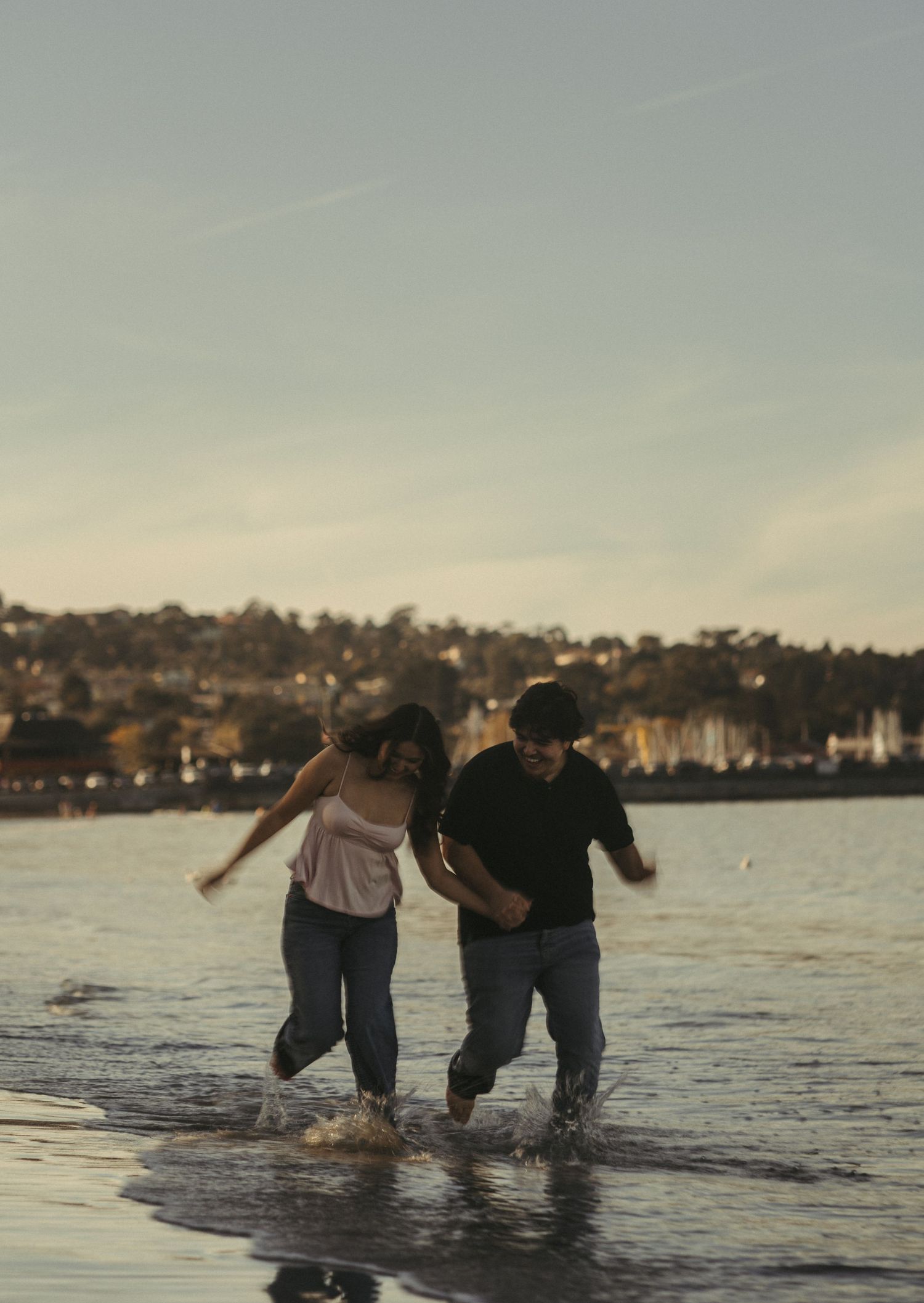 Couple running through the beach water splashing during their couple's photo session in Monterey