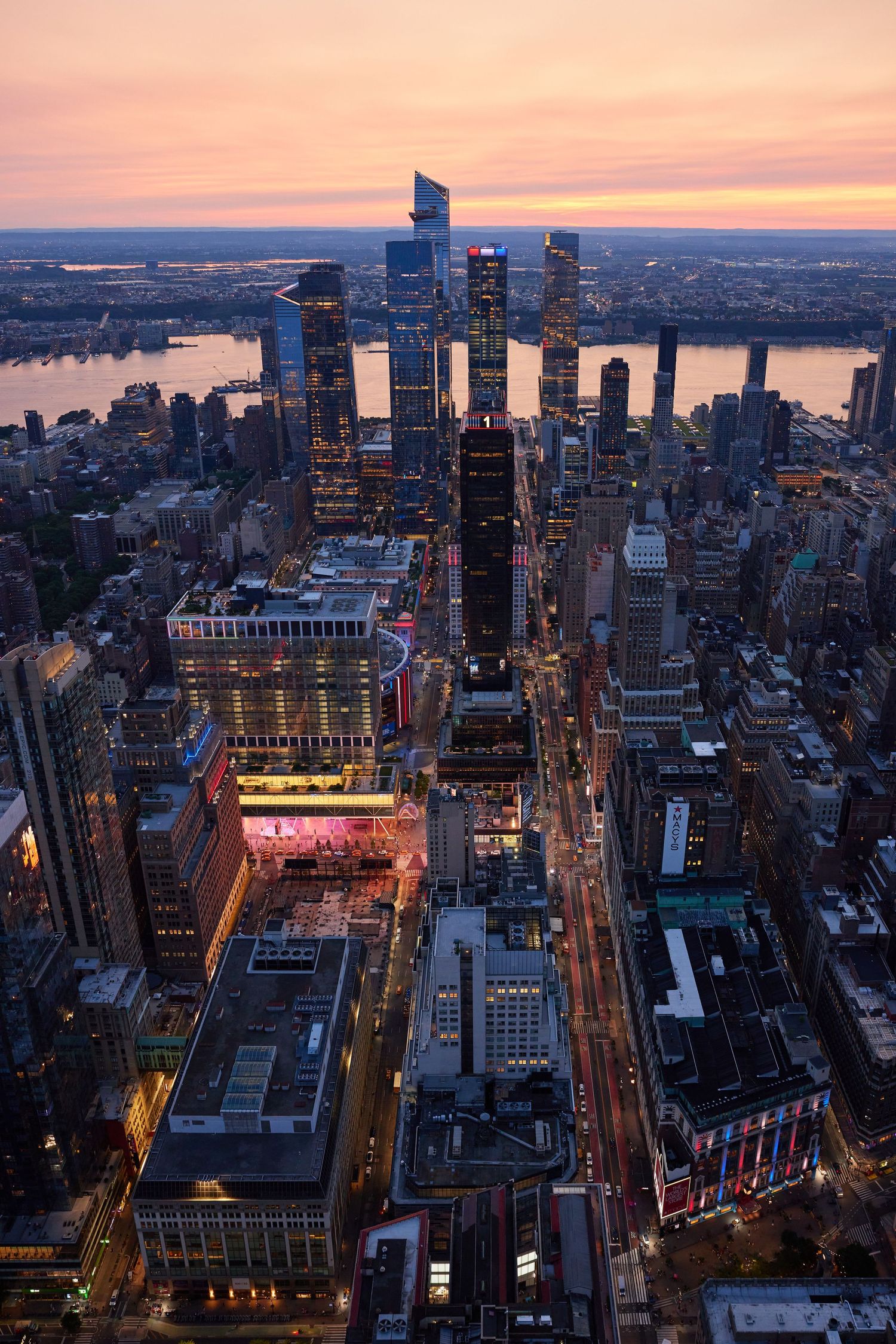 Aerial view of Midtown Manhattan at sunset, skyscrapers and city streets stretching toward the Hudson River.