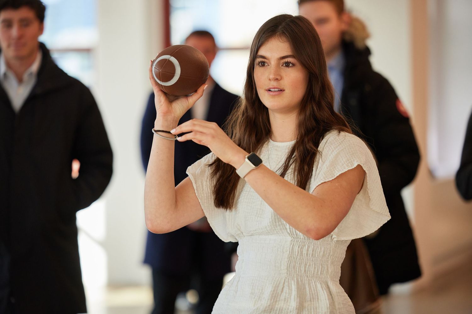 Woman holding football during indoor lifestyle activation with attendees in background