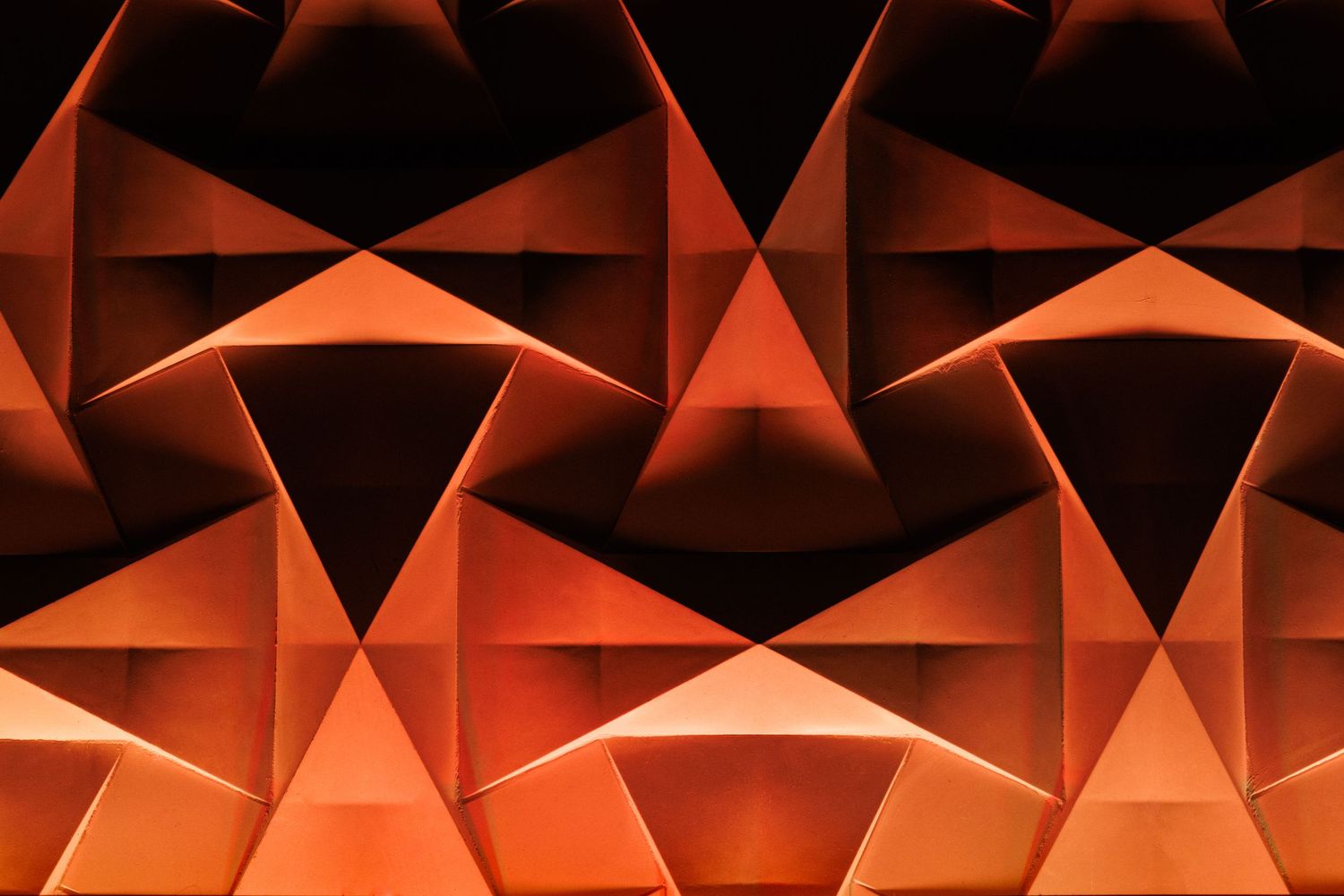 Abstract architectural pattern of illuminated triangular surfaces forming warm geometric reflections.