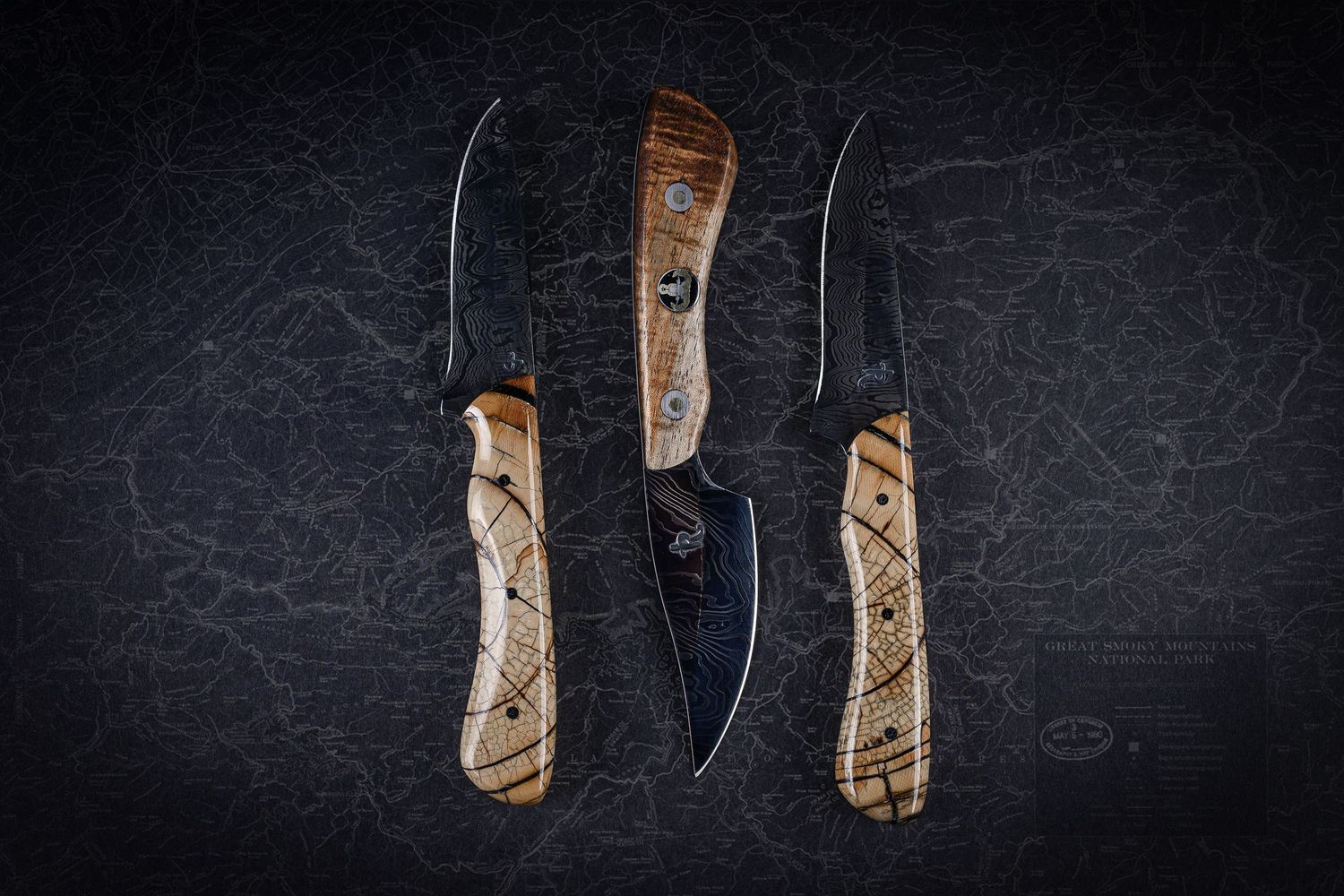 Three handcrafted knives with spalted wood handles displayed on dark textured background.