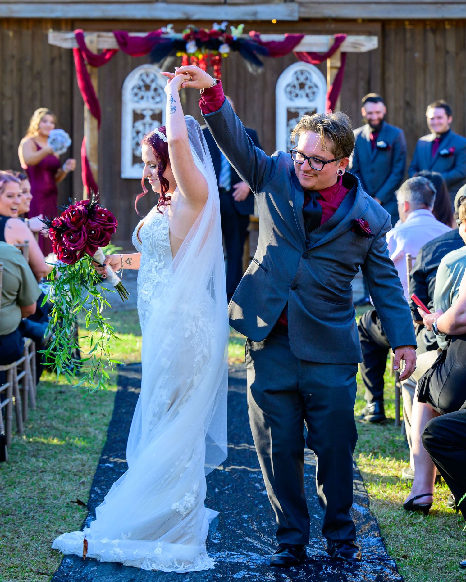 Joyful bride and groom raise hands walking back down aisle after outdoor barn wedding ceremony.