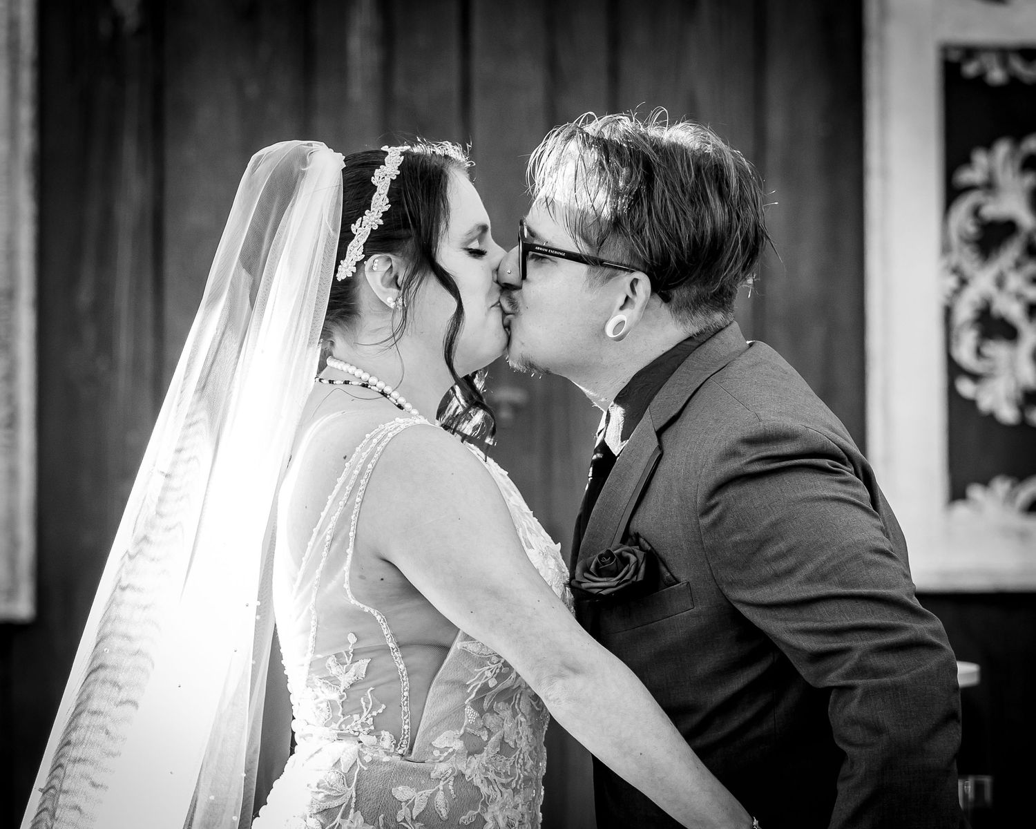 Black and white photo of bride and groom sharing first kiss at wedding ceremony.
