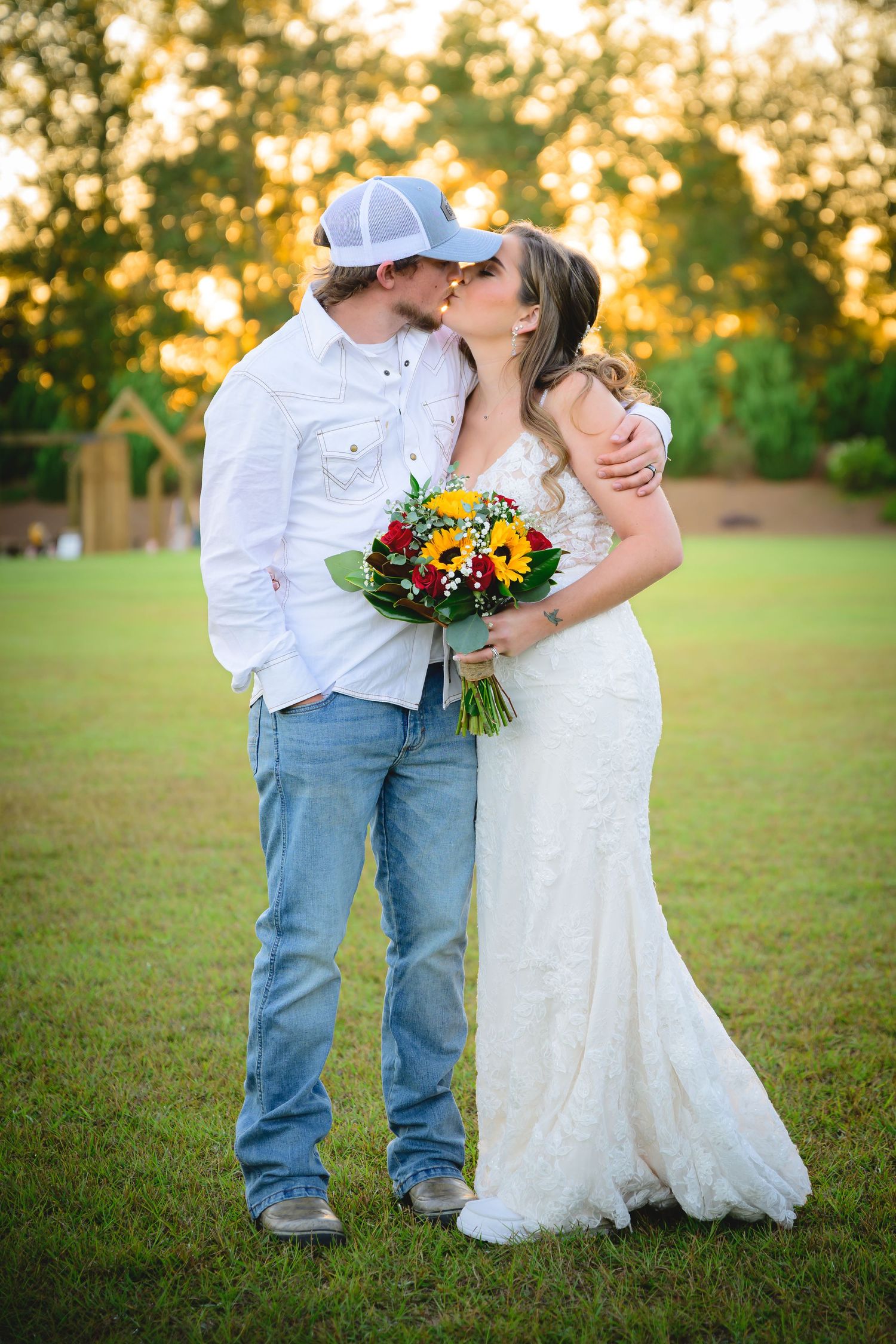 Bride and groom kissing at sunset holding a colorful sunflower and wildflower wedding bouquet.