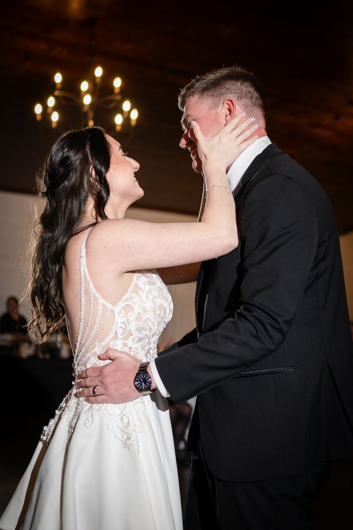 Bride and groom share intimate first dance at romantic chandelier-lit wedding reception.