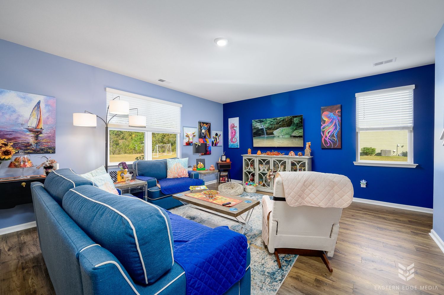 Vibrant blue-walled living room with blue sofa, colorful artwork, and hardwood floors.