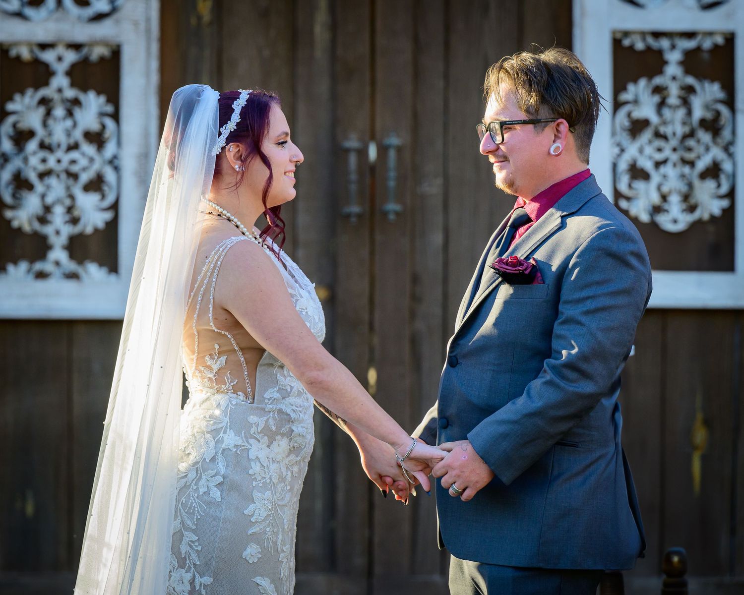Bride and groom exchange vows holding hands at outdoor rustic barn wedding ceremony.