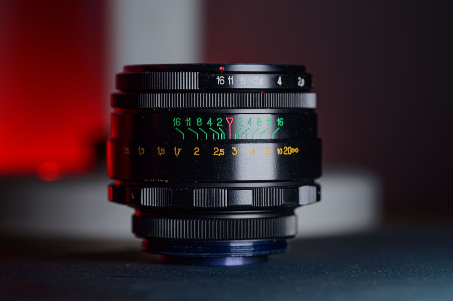 Side view of a vintage black camera lens showing colorful aperture and focus markings.