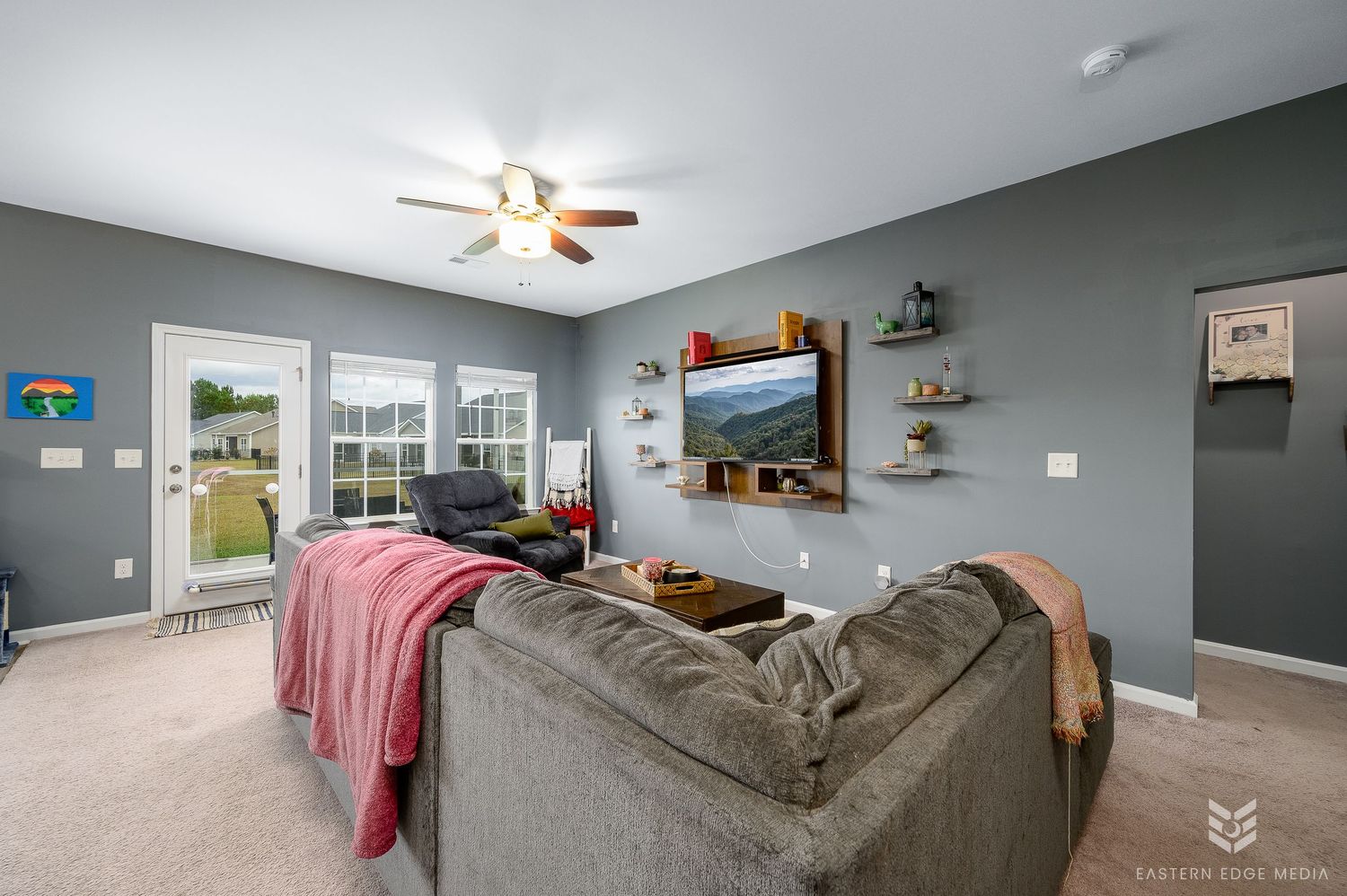 Gray living room with ceiling fan, sofa, wall shelves, and French doors to backyard.
