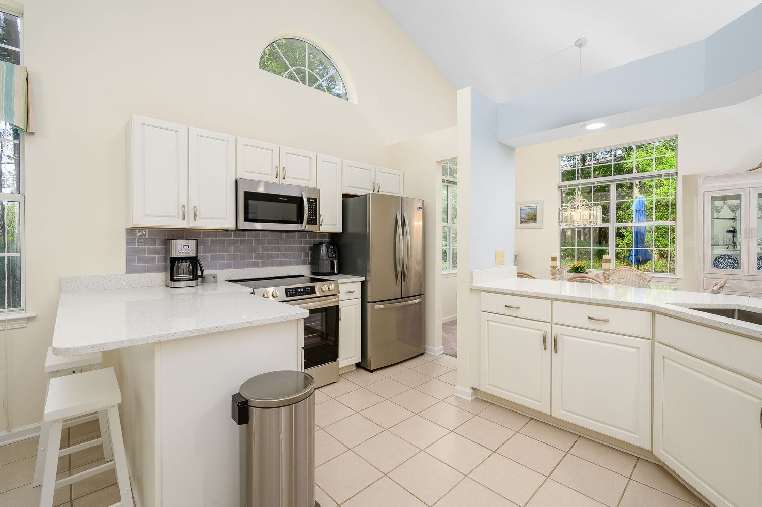 Bright white kitchen with stainless steel appliances, tile floors, breakfast bar, and vaulted ceiling.