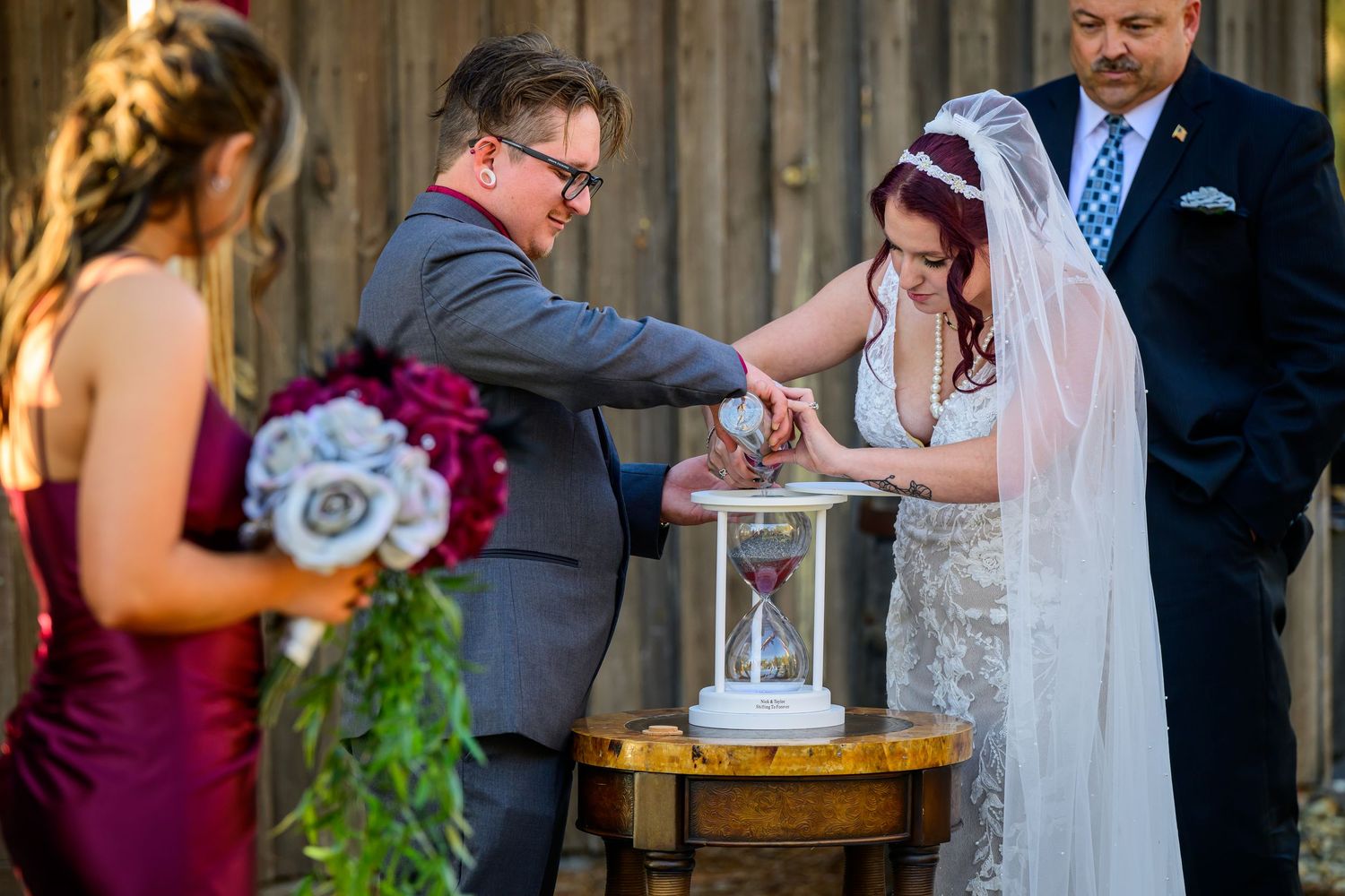 Bride and groom pour sand together in unity ceremony at outdoor rustic barn wedding.