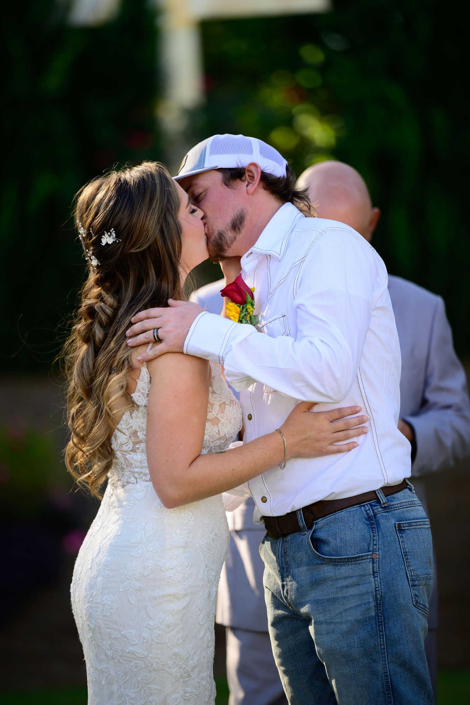 Bride and groom sharing their first kiss at an outdoor wedding ceremony with lush greenery.