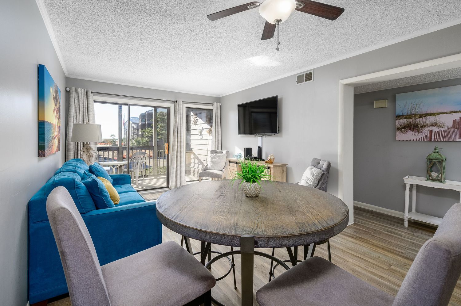 Open dining and living area with ceiling fan, blue sofa, round table, and balcony access.