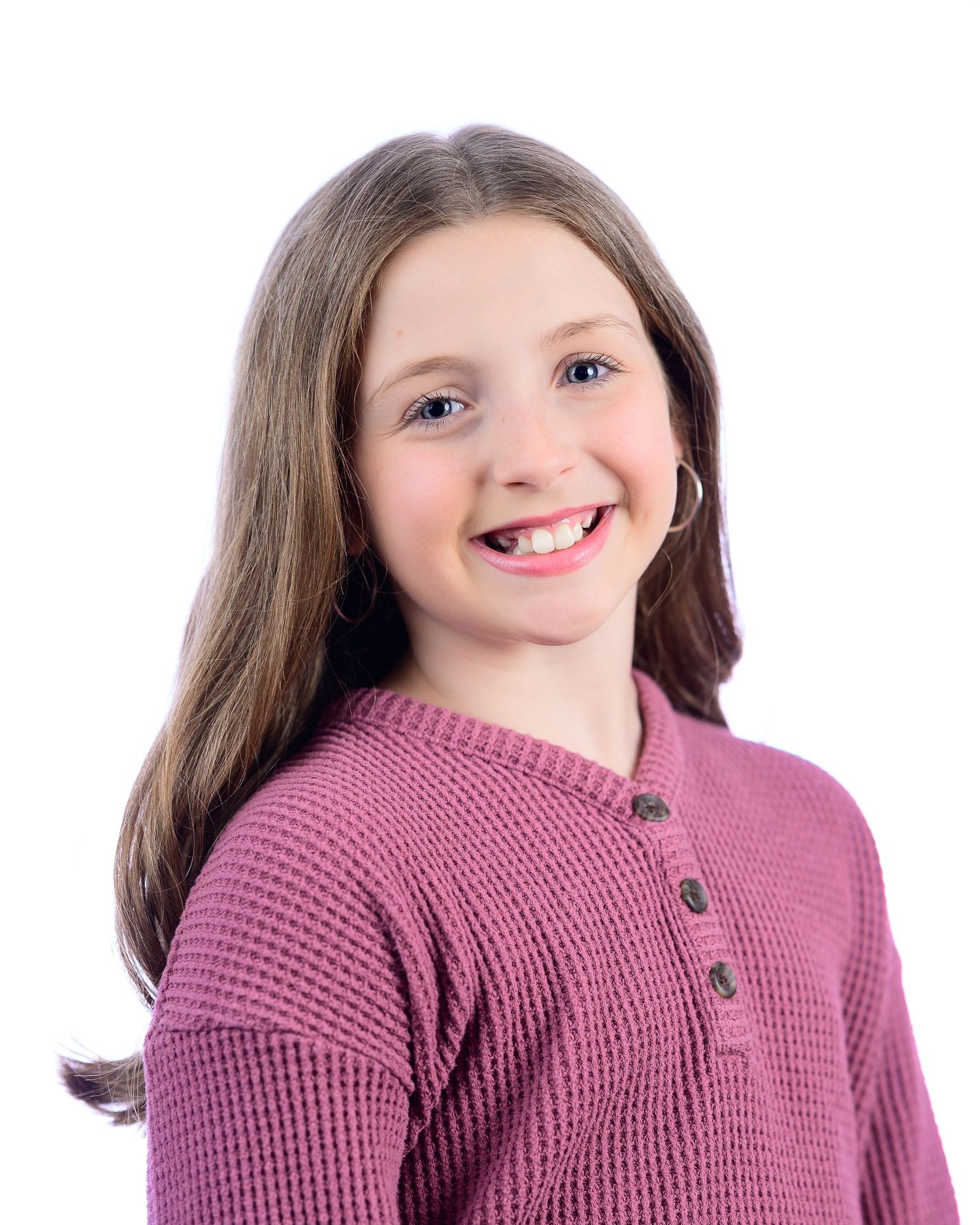 Cheerful young girl in pink waffle knit top smiles in bright studio portrait.