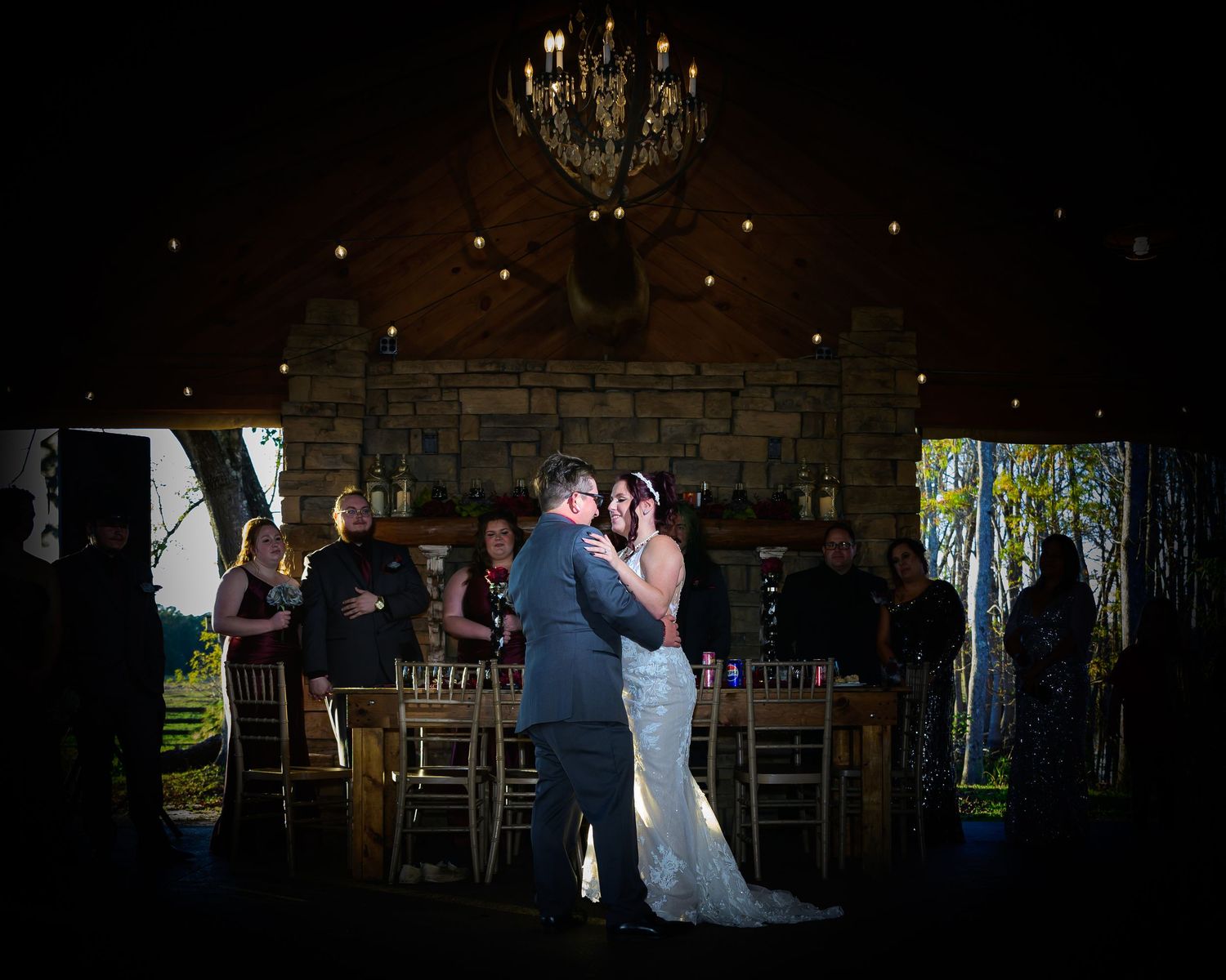 Bride and groom share first dance under chandelier in rustic stone wedding venue at night.