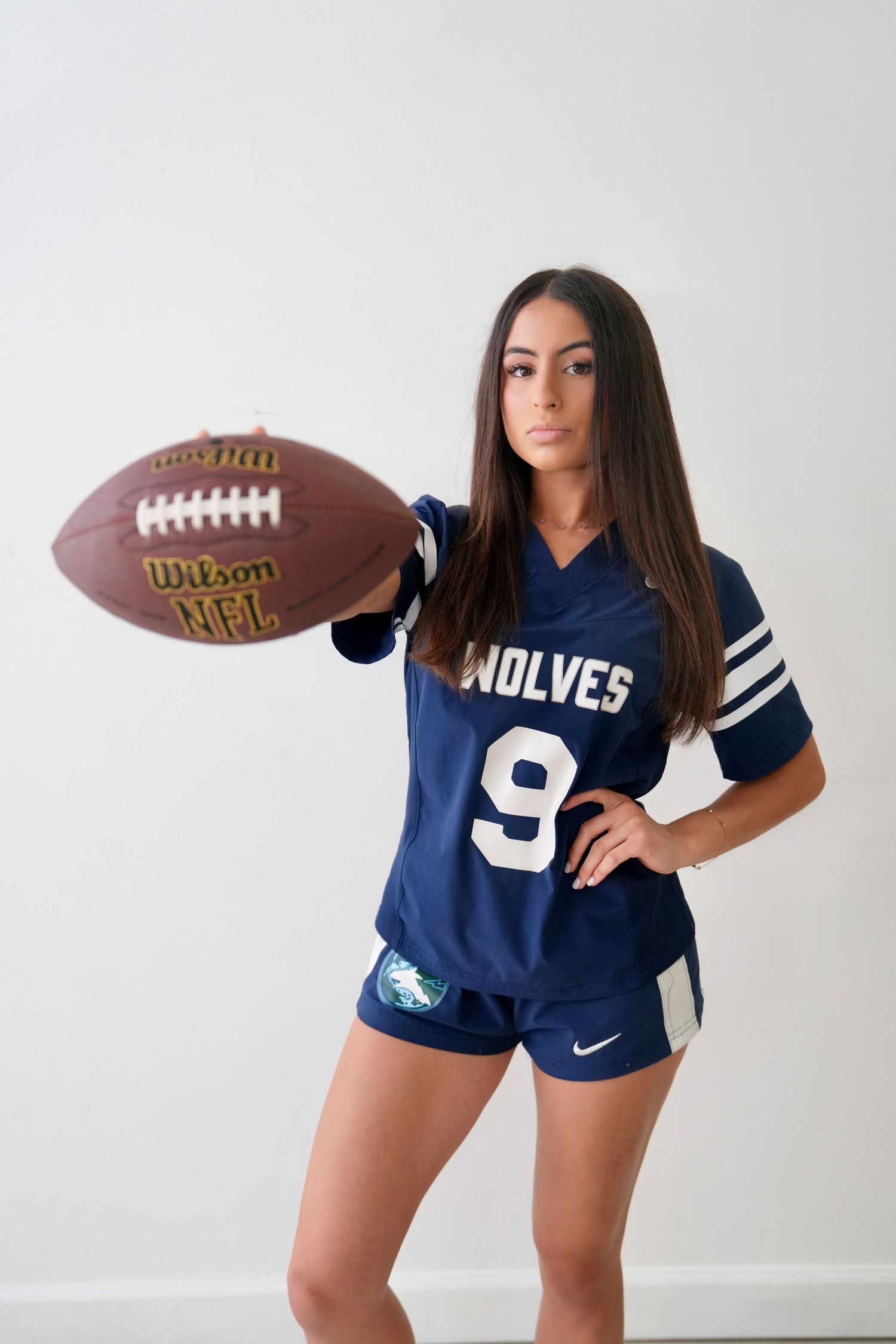 Teen girl in Wolves number 9 football jersey holds Wilson NFL ball confidently.