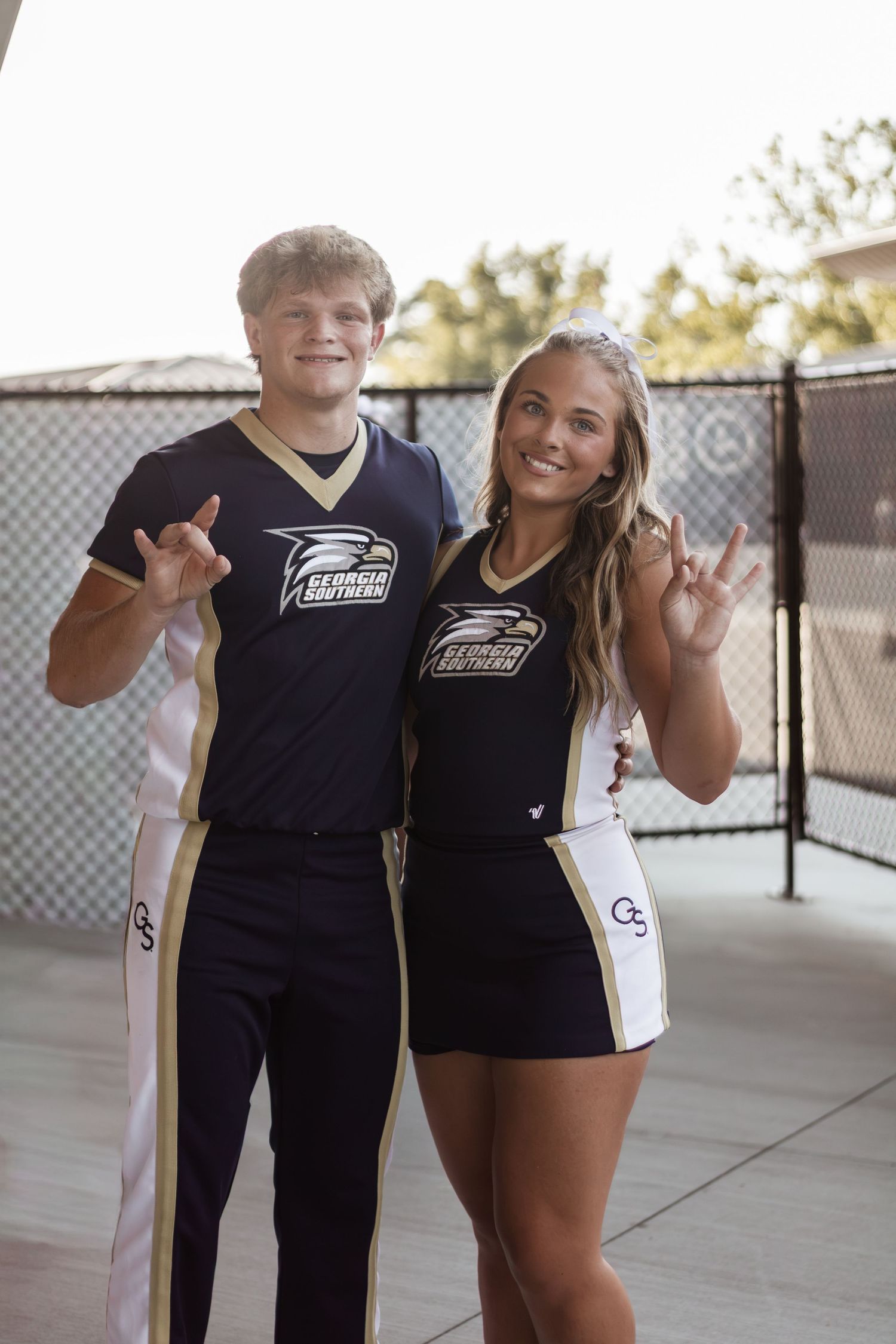 Two young adults in matching Georgia Southern University uniforms posing together making hand signs.