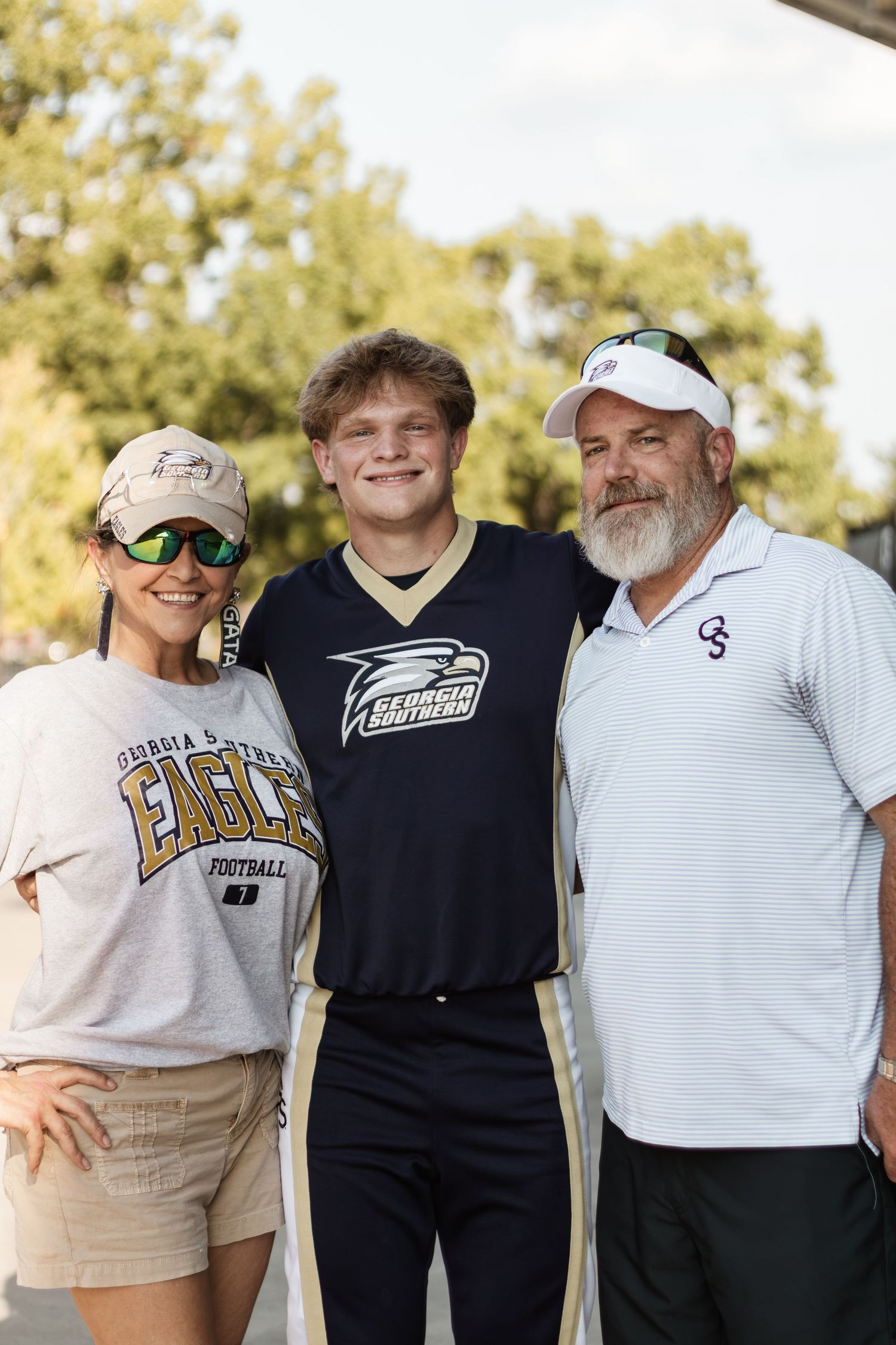 Family of three posing together wearing Georgia Southern Eagles football apparel at a stadium event.