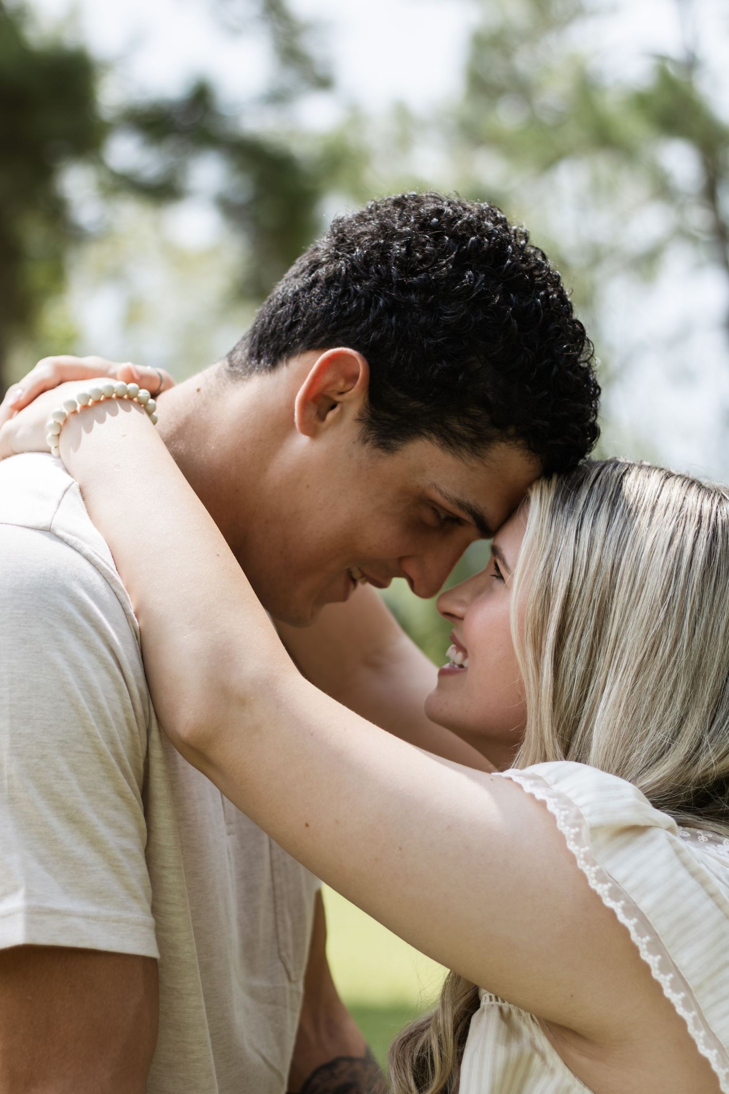 A young couple shares a romantic forehead-to-forehead moment while embracing outdoors in a park.