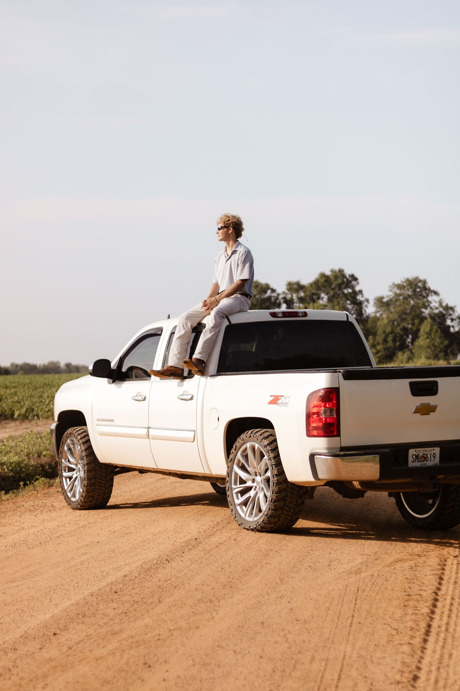 Young man sitting on top of a white Chevrolet Z71 pickup truck on a rural dirt road.