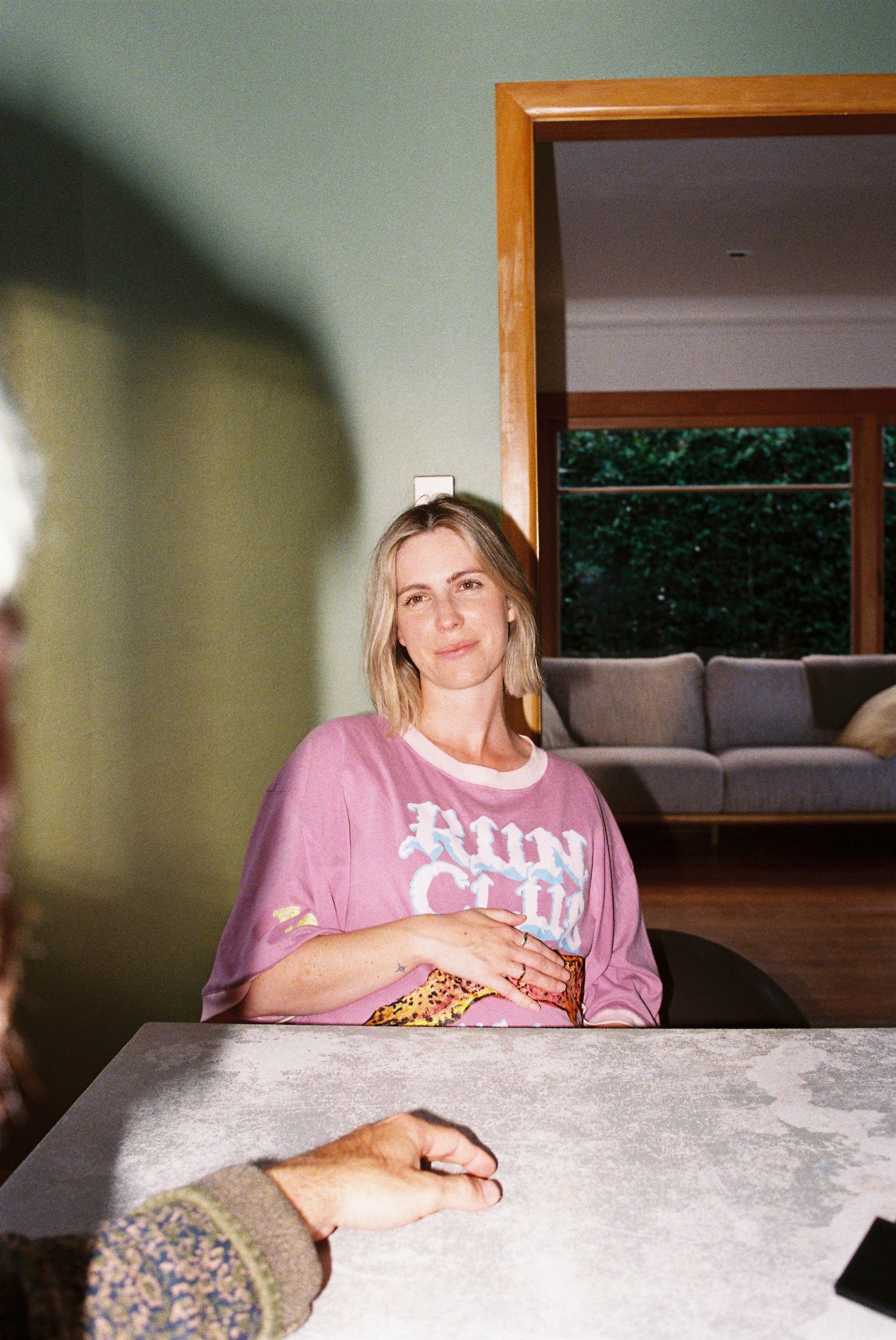 Woman in pink Run Club t-shirt sitting at a marble table in a cozy living room.