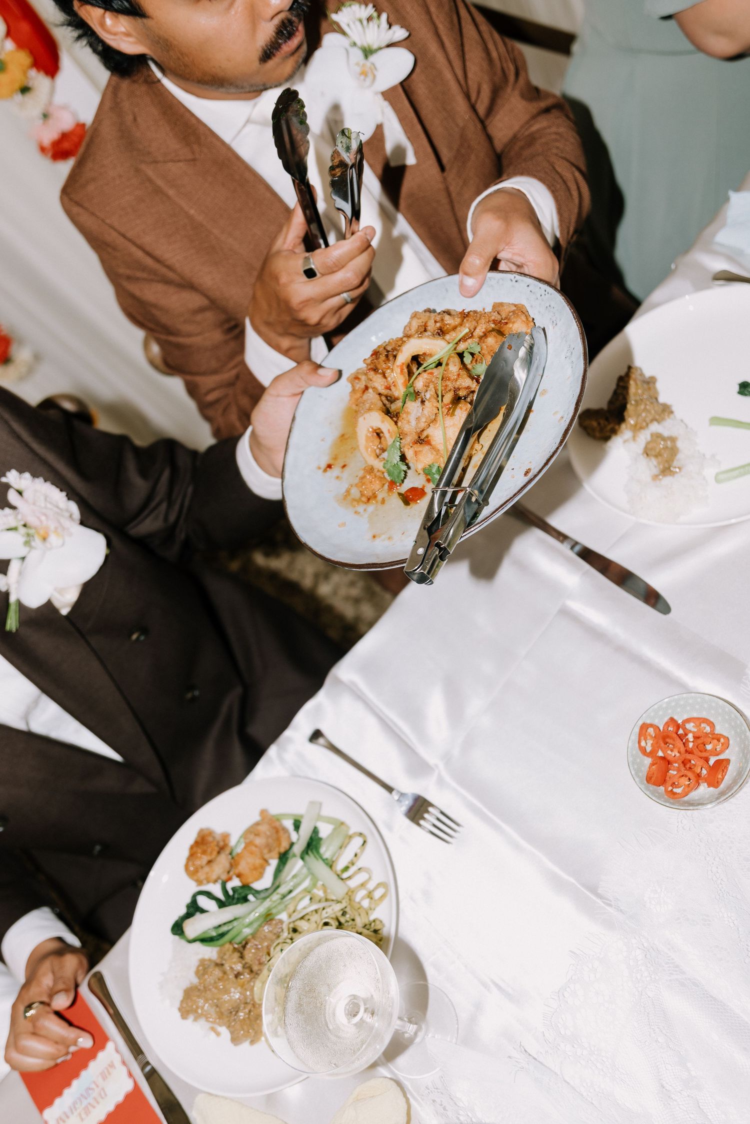Wedding guests serve themselves food at a white tablecloth reception dinner from above.