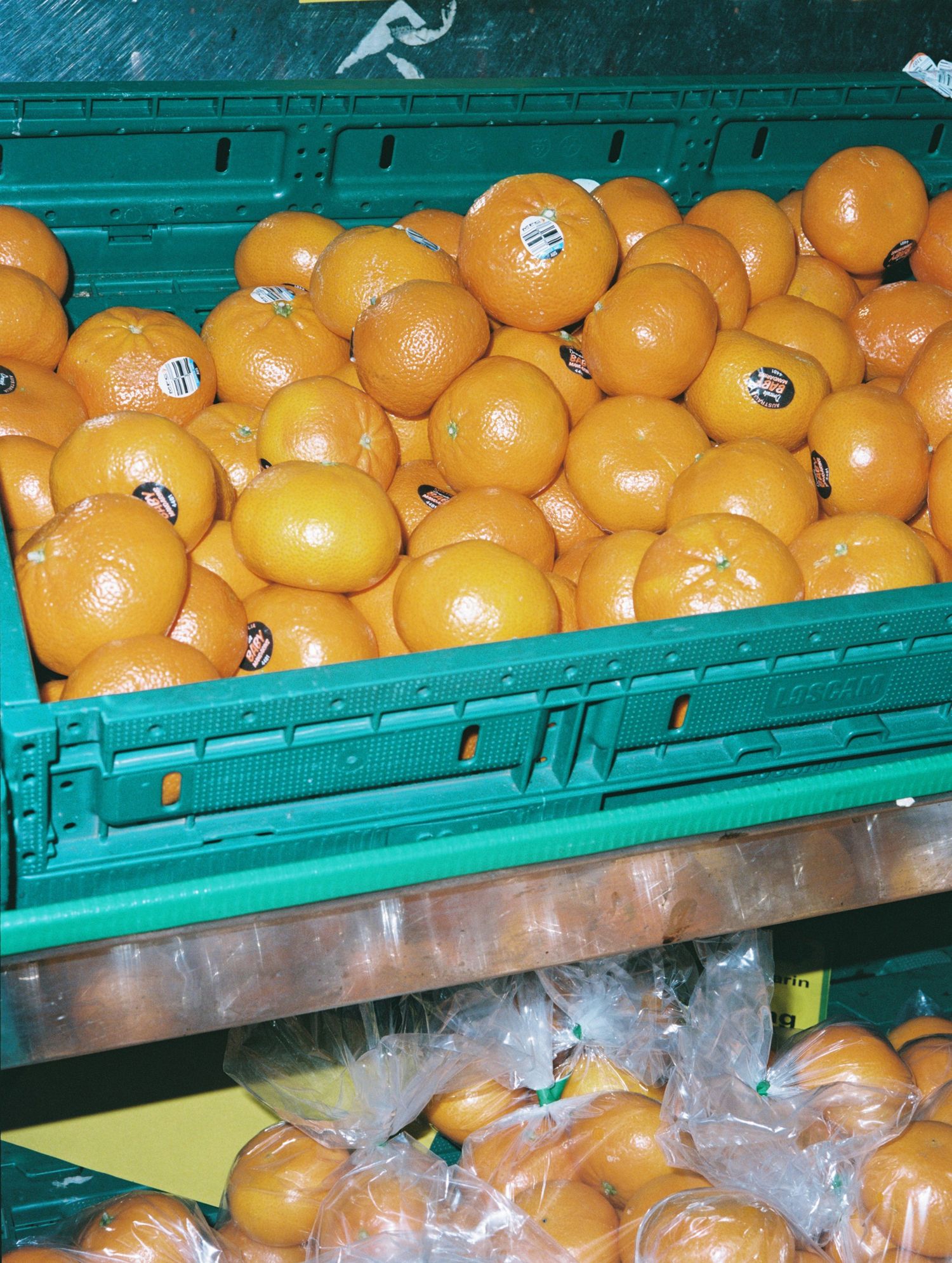 Fresh oranges displayed in green produce crates at grocery store market shelf.