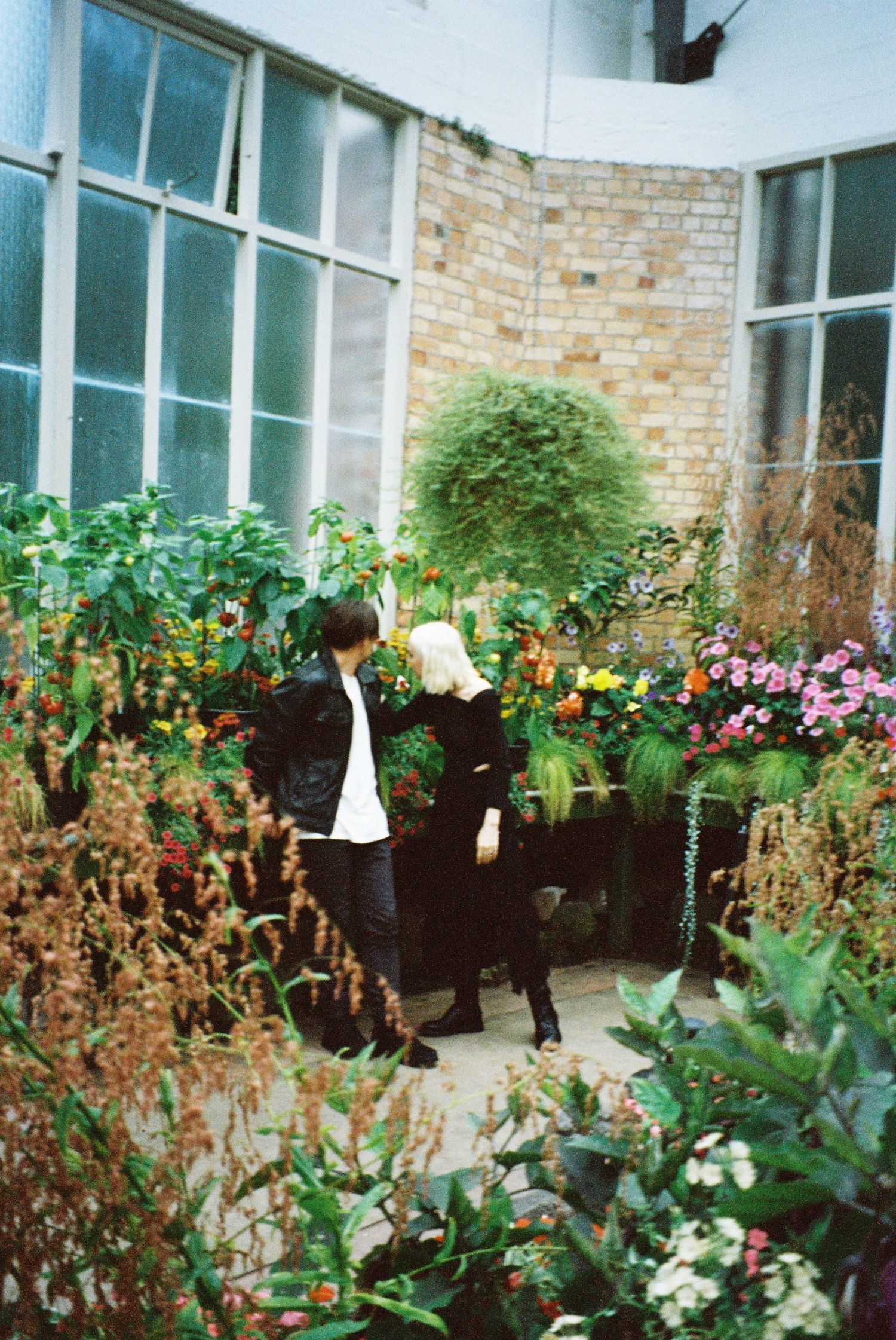 Couple surrounded by lush colorful flowers and plants in a greenhouse garden courtyard setting.