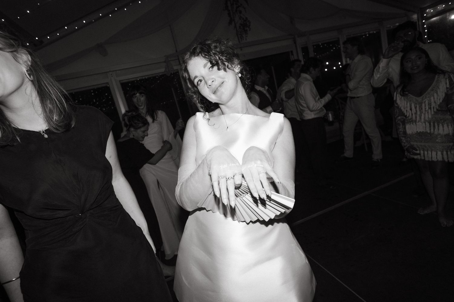 Black and white photo of bride dancing joyfully at wedding reception under tent lights.