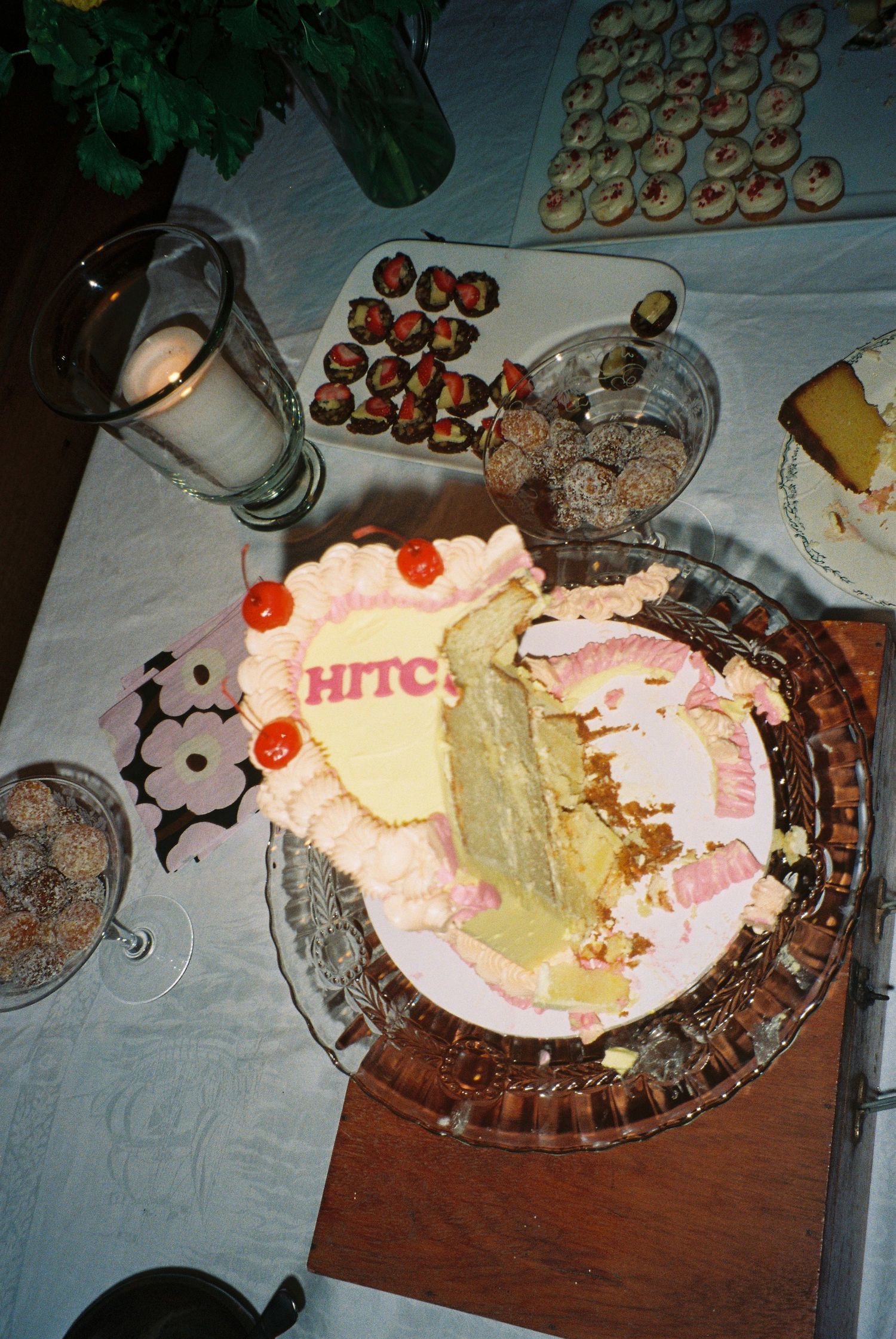 Partially sliced wedding cake labeled HITC surrounded by chocolate strawberries and cupcakes.