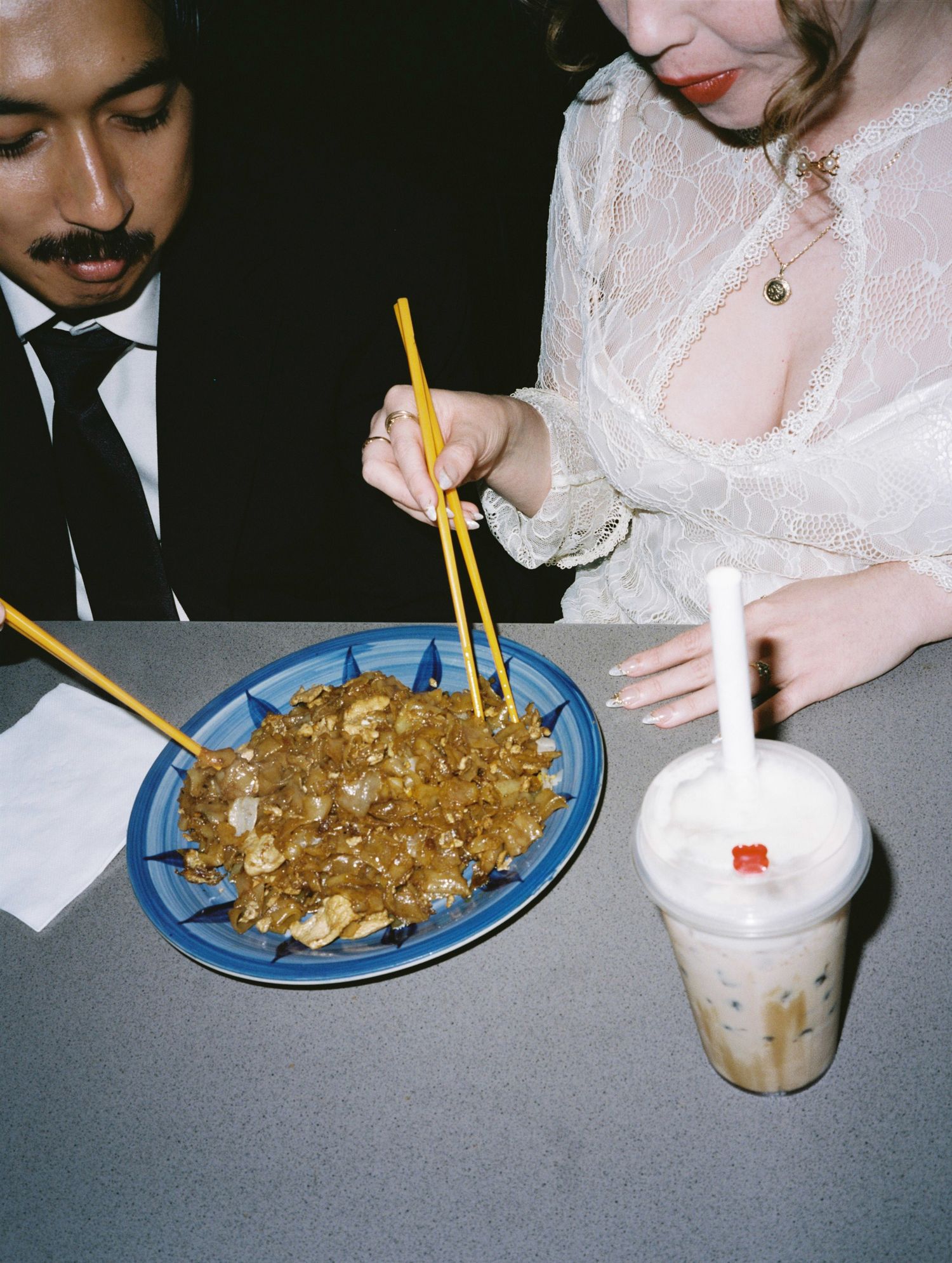 Wedding couple sharing fried rice with chopsticks and bubble tea at casual late-night reception dinner.