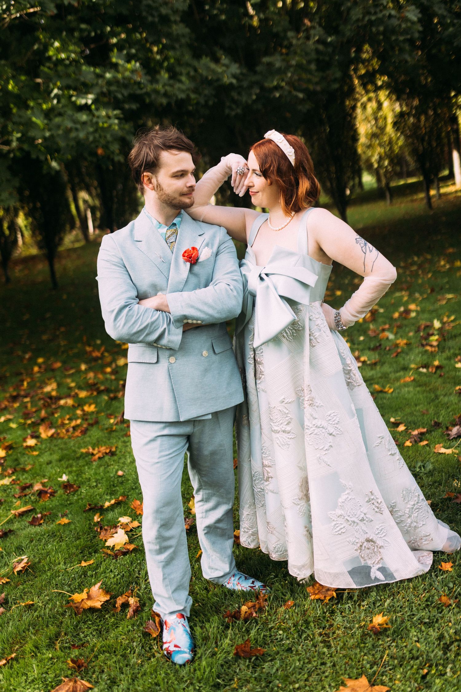 Bride in light blue embroidered gown and groom in matching suit share a tender moment in autumn park.