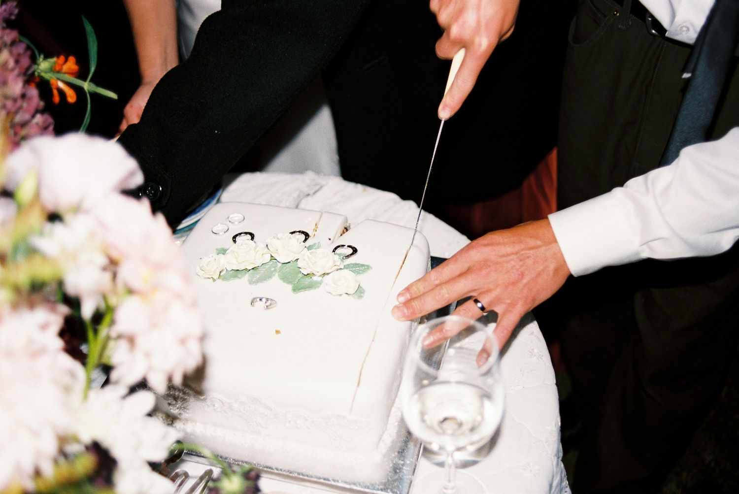 Bride and groom cutting white wedding cake decorated with floral designs at reception.