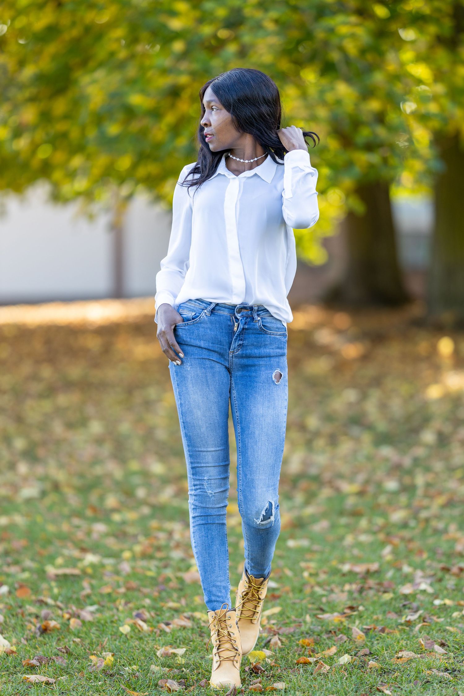 Jacky steht in weißer Bluse und Jeans zwischen herbstlichen Bäumen