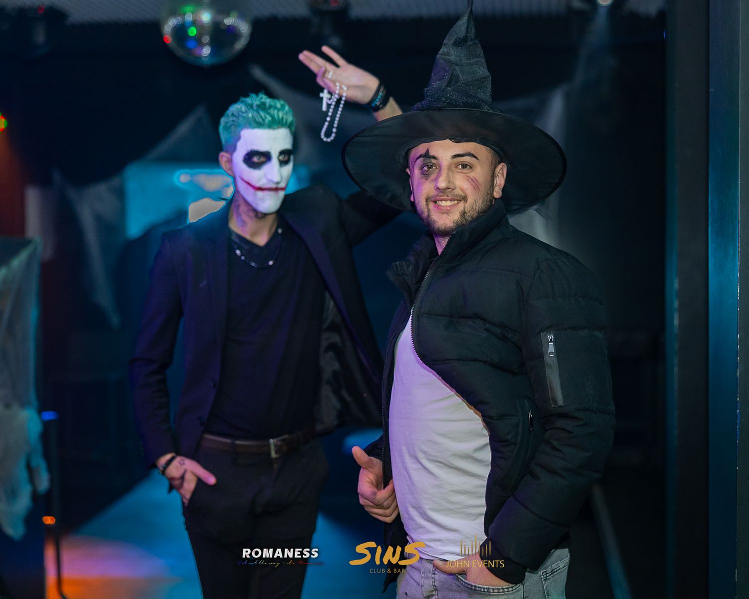 Zwei verkleidete Männer mit Gesichtsschminke und Hexenhut stehen im Club Sins zusammen.