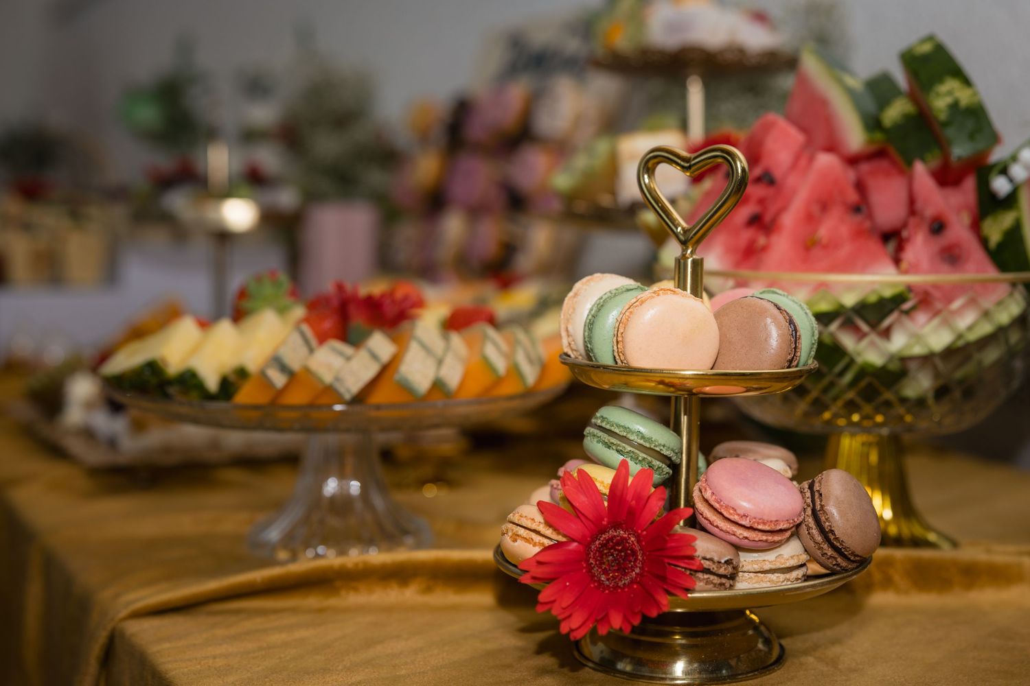 Macarons und eine rote Blüte stehen auf einer Etagere vor dem Obstbuffet der Tauffeier.