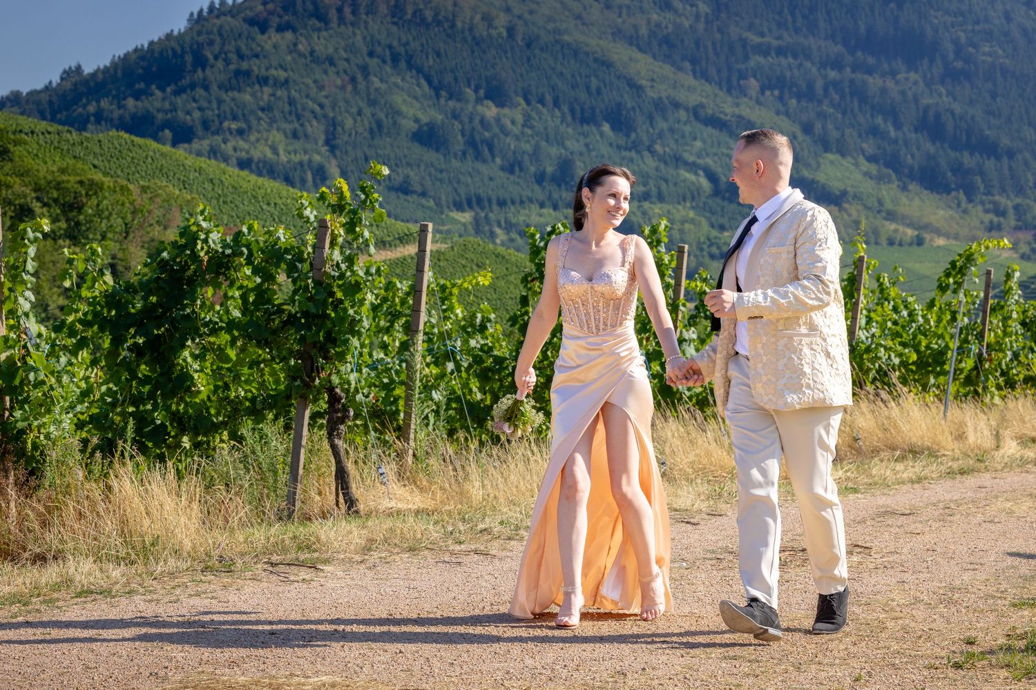 Brautpaar geht Hand in Hand auf einem Weg zwischen den Weinbergen