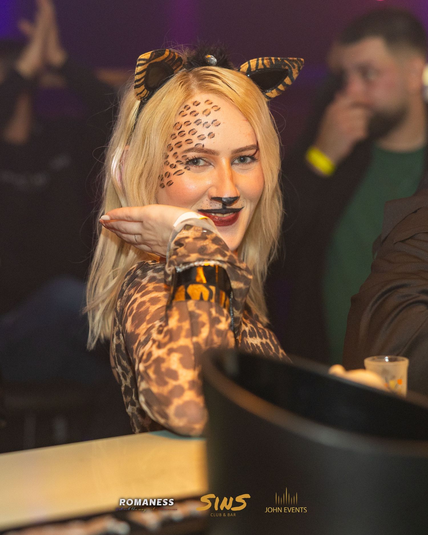 Eine blonde Frau mit Katzenohren und gemustertem Halloween-Make-up hält ihre Hand vor dem Gesicht im Sins.