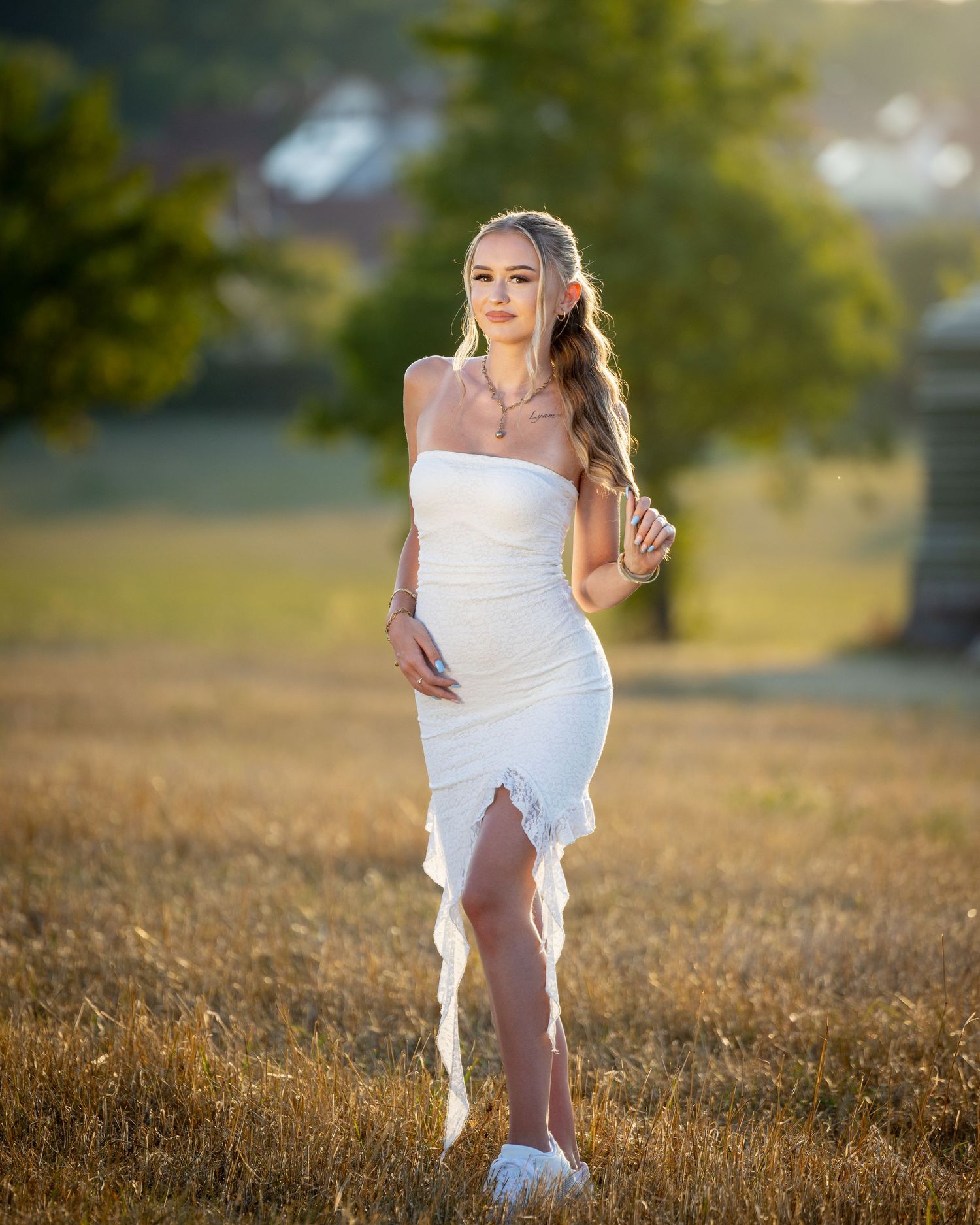 Cătălina steht in einem weißen schulterfreien Kleid im Feld; das Sonnenlicht zeichnet ihr Haar von hinten nach.