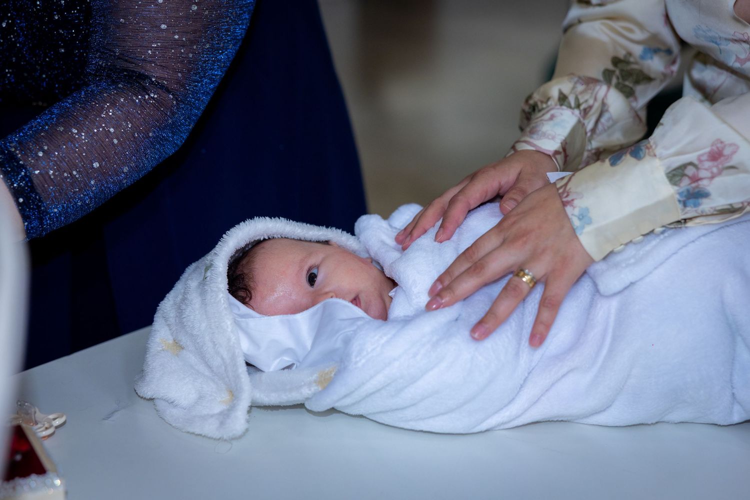Newborn baby swaddled in white blanket held gently by adult hands during a tender moment.
