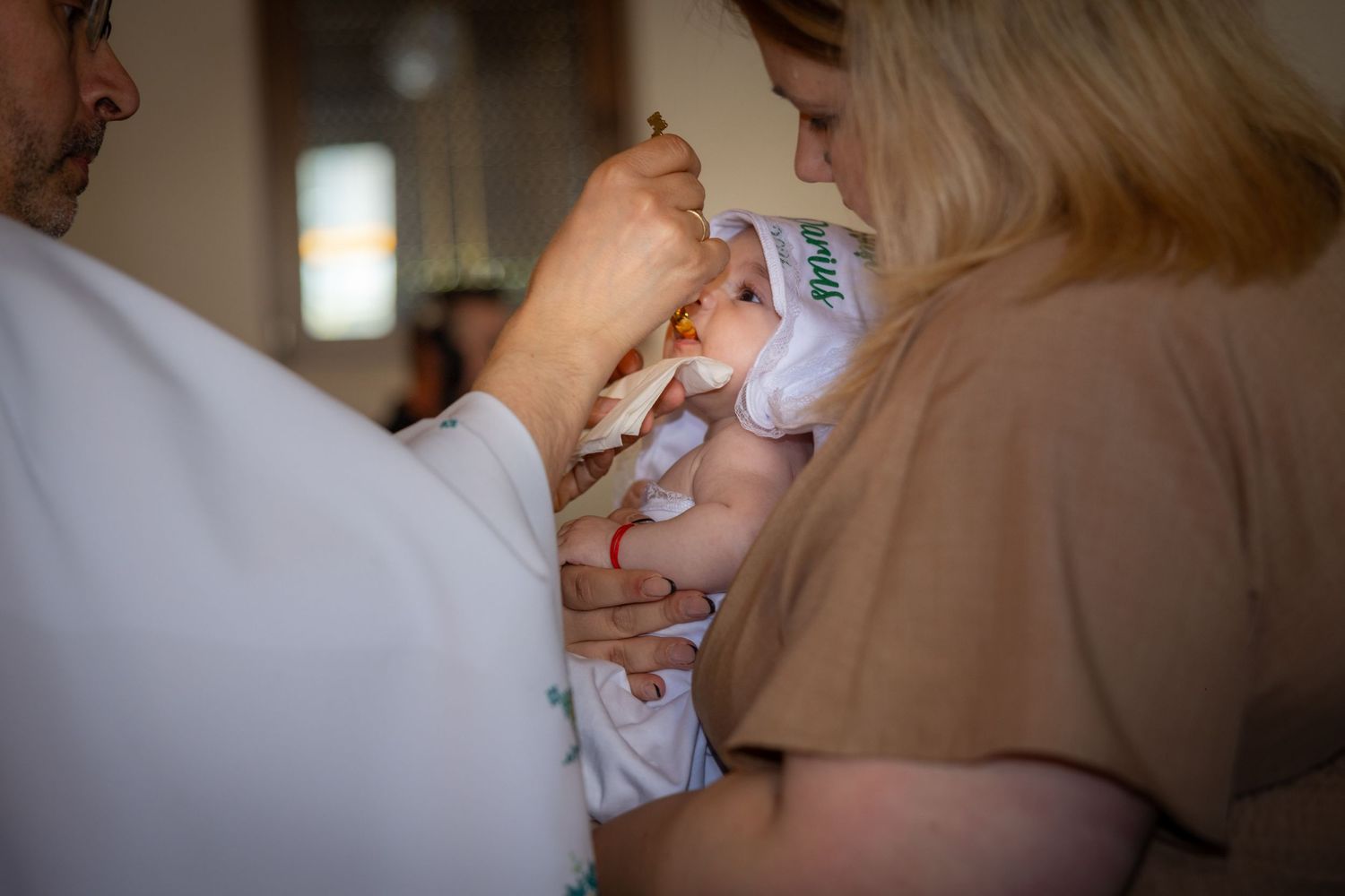 A baby being fed with a bottle by two adults during an intimate feeding moment indoors.