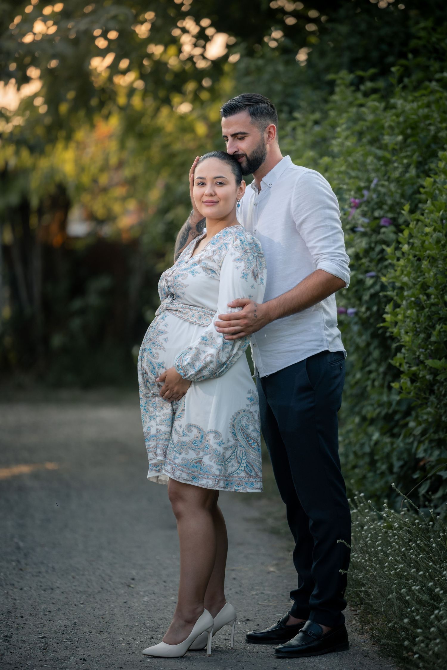 Cristina steht im gemusterten Kleid vor Claudiu, der eine Hand an ihren Bauch legt.