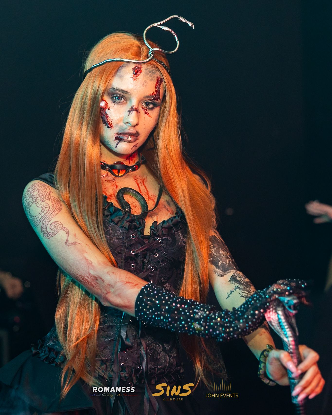 Eine Frau mit langen orangefarbenen Haaren, aufwendigem Halloween-Make-up und schwarzem Kostüm im Sins.