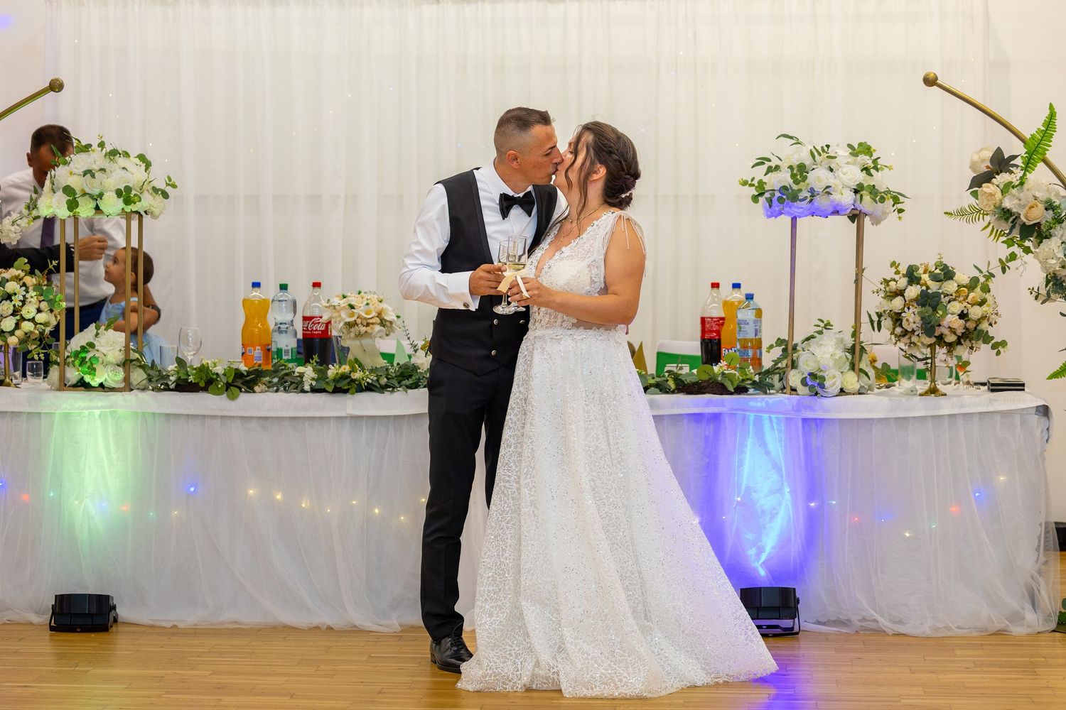 Das Hochzeitspaar küsst sich vor dem dekorierten Brauttisch.