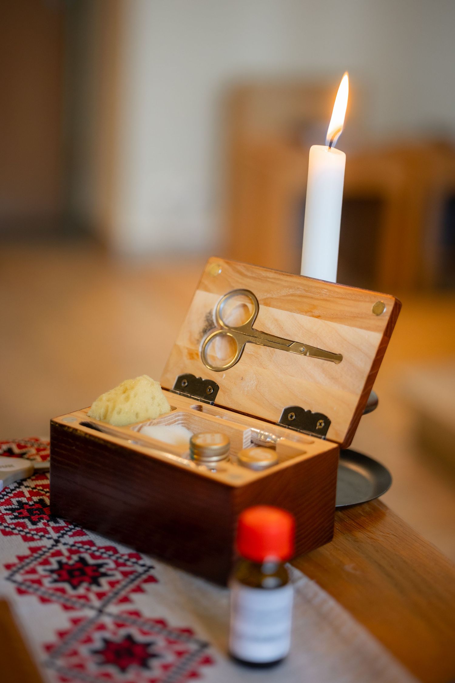 Eine brennende Taufkerze neben einer geöffneten Holzschatulle mit Schere und weiteren Ritualgegenständen.