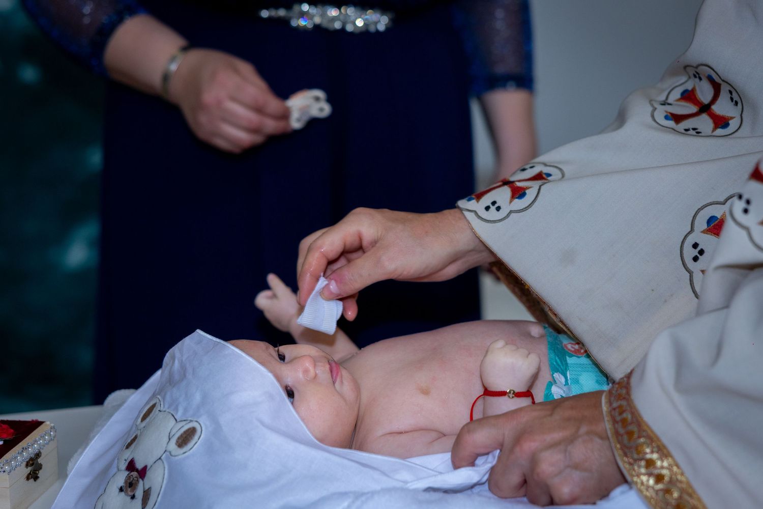 Priest performing a Christian baptism ceremony on a newborn baby wrapped in white cloth.