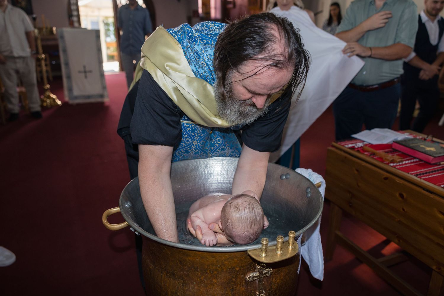 Der Priester hält Theodor während der Taufe im metallenen Taufbecken.