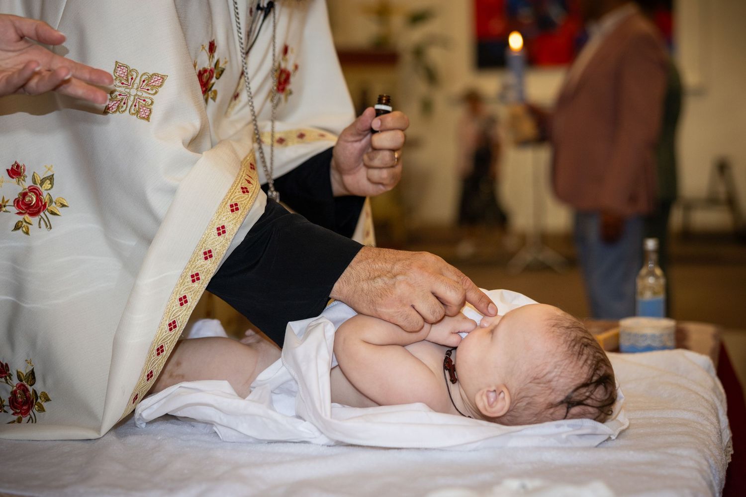 Der Priester berührt Aris’ Gesicht bei der Salbung, während das Kind in einem weißen Tuch liegt.
